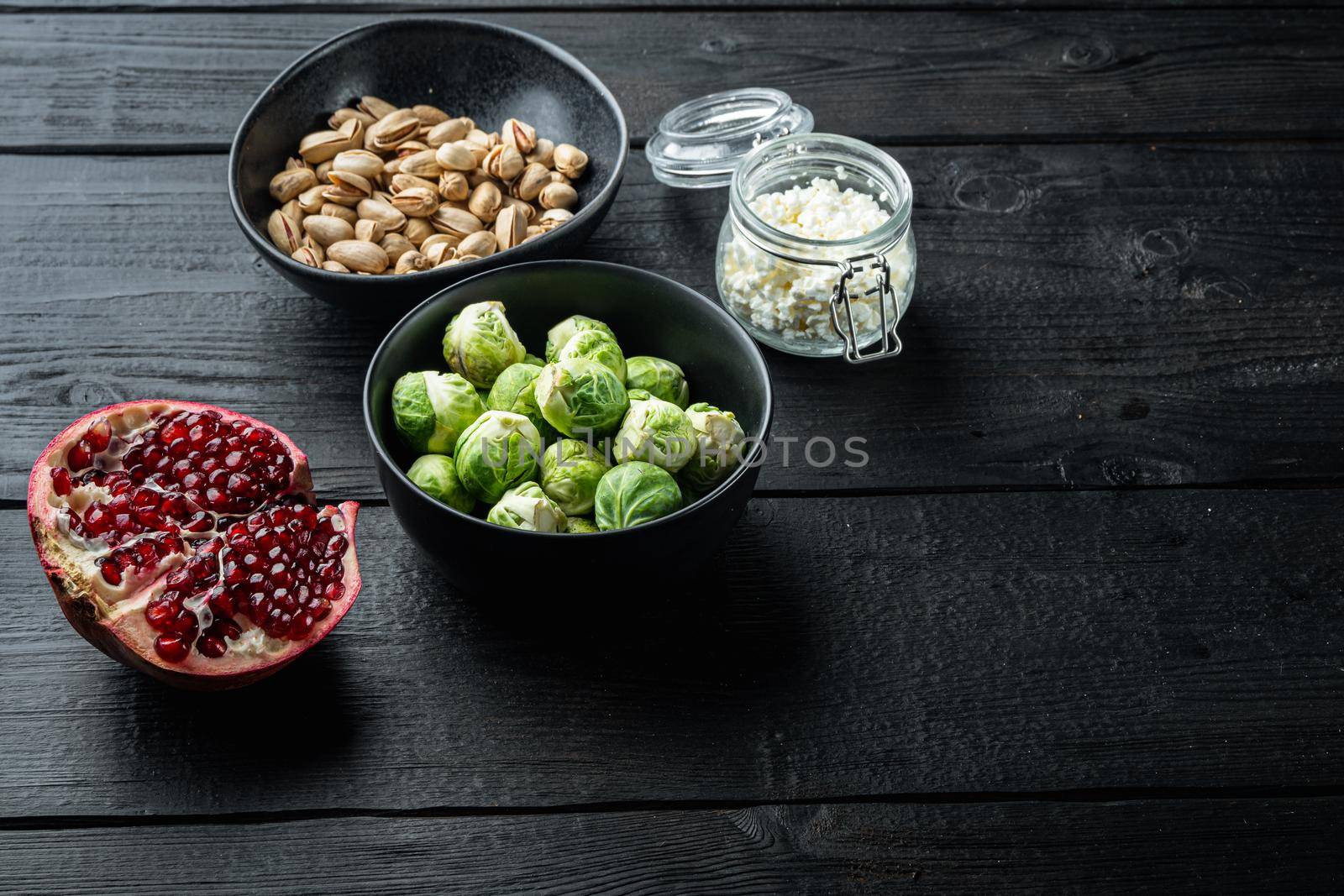 Brussels sprouts with pomegranate, cottage cheese and pistachios, on black wooden table with space for text