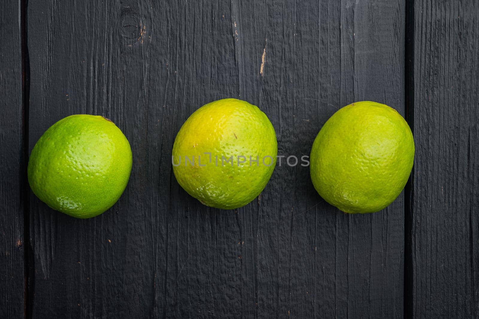 Ripe green lime set, on black wooden background, top view or flat lay