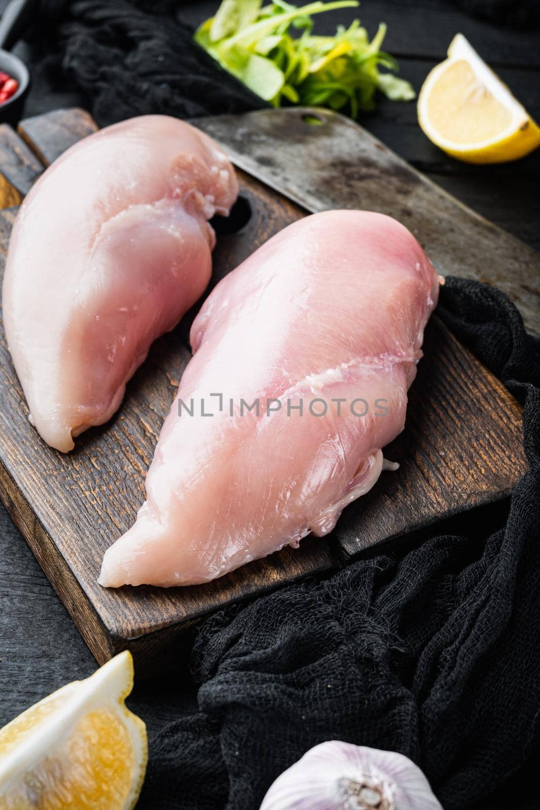 Raw crumbet chicken fillet with ingredient with butcher knife on black wooden table