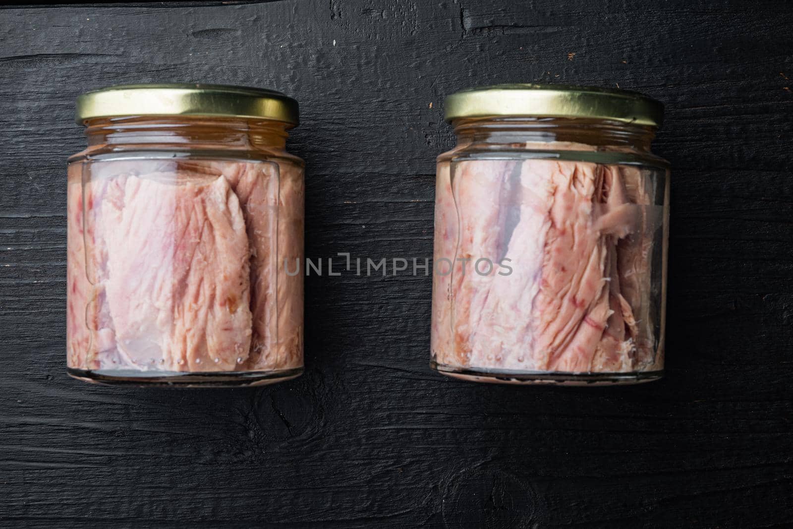 Tuna fillet meat in glass jar, on black wooden background, flat lay