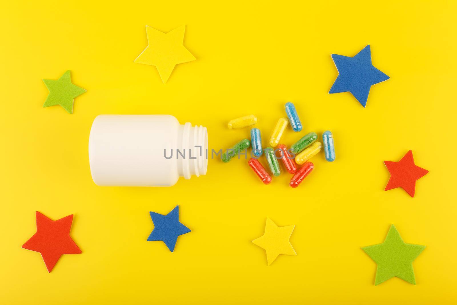 Flat lay with medication bottle with spilled multicolored pills on yellow background decorated with stars.Concept of wellness, healthy lifestyle or vitamins for kids