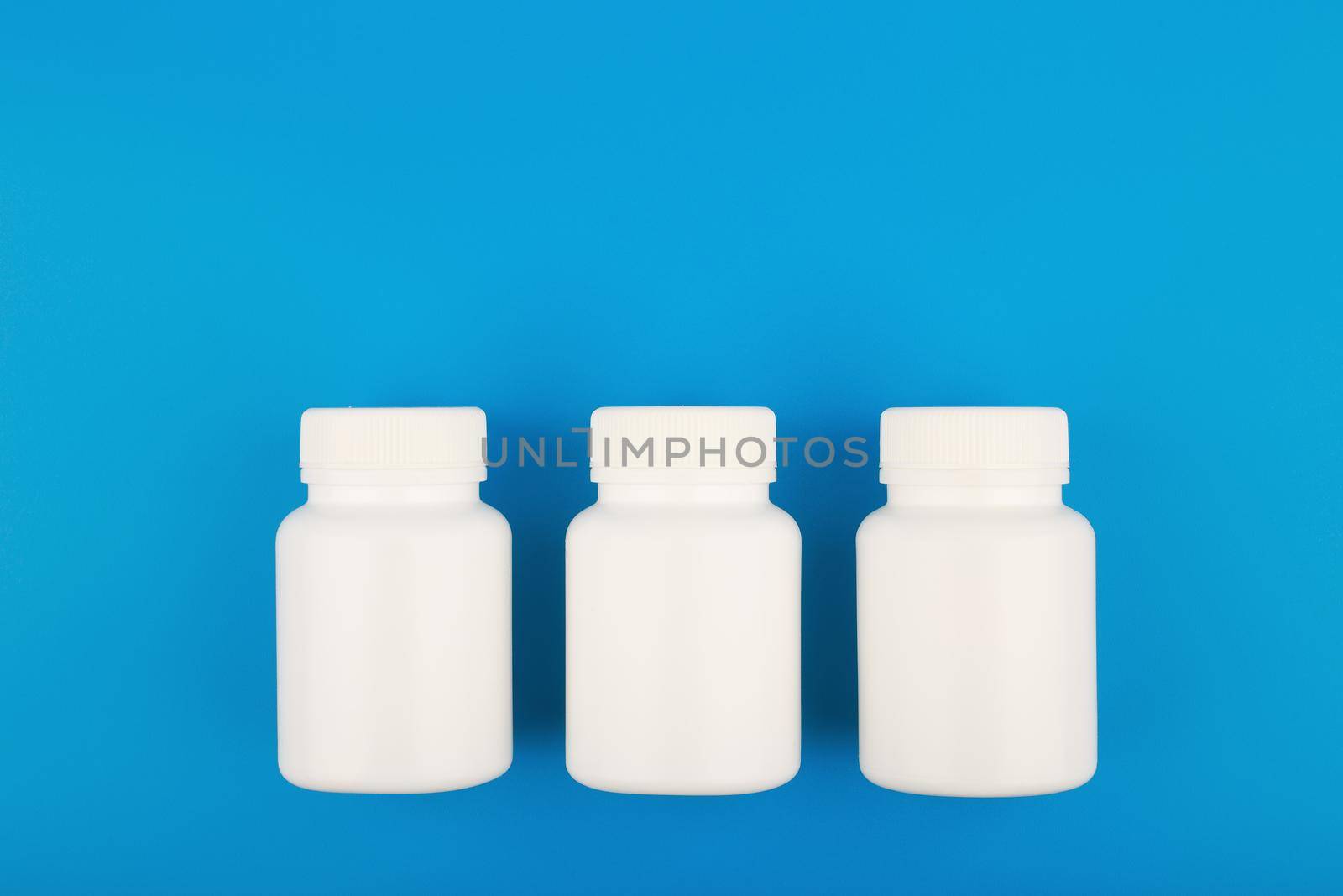 Flat lay with three white medication bottles in a row on blue background with copy space by Senorina_Irina