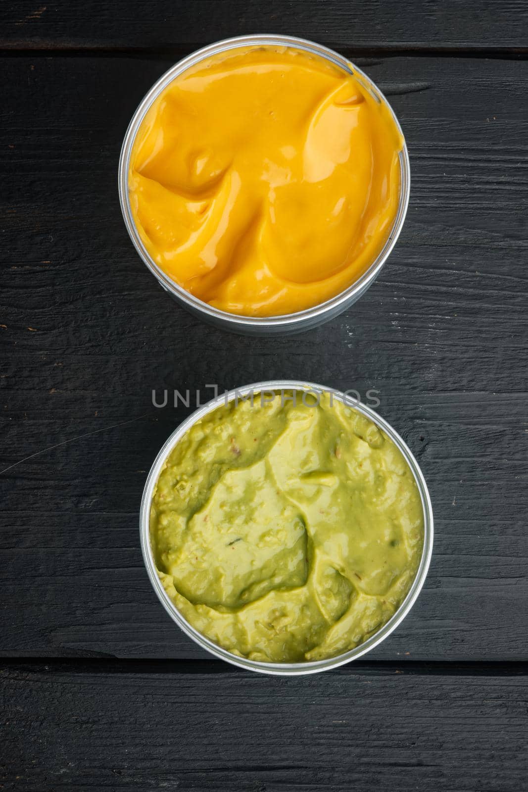 Canned cheese and guacamole sauce in can, on black wooden background, top view or flat lay