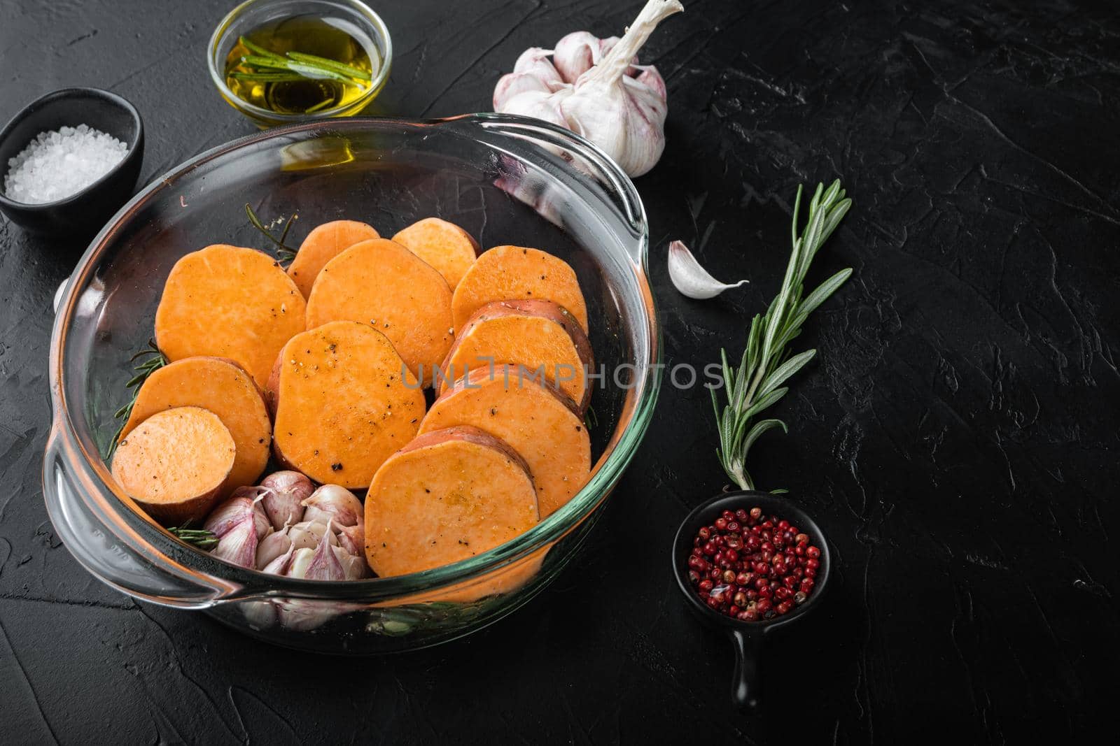 Cajun sweet potatoes for baking with herbs and spices on black background.