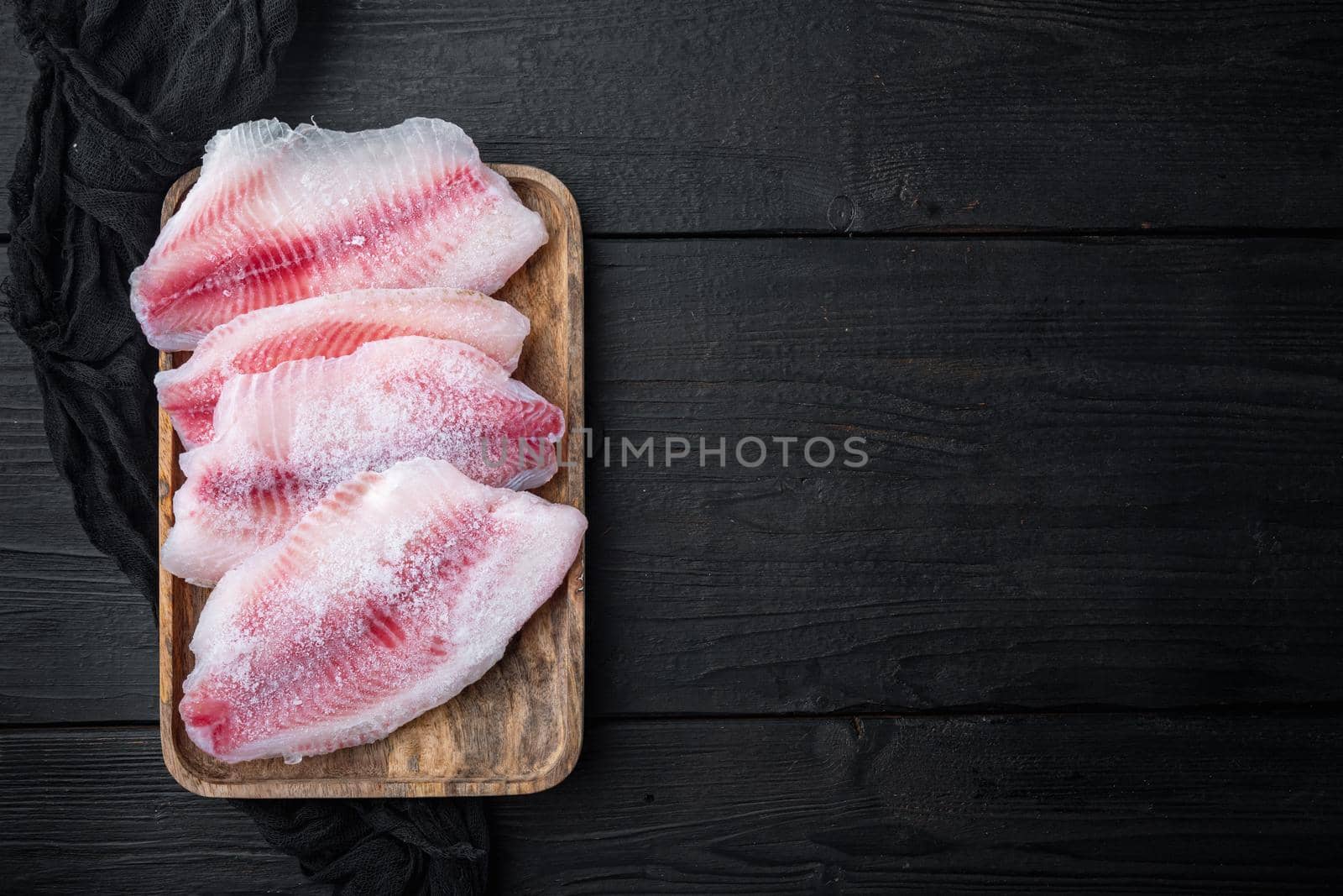 Frozen, white fish fillet, on black wooden background, top view with copy space for text