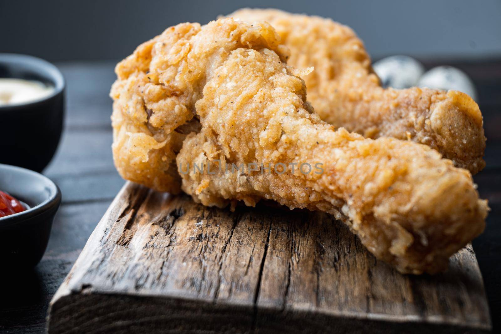 Fried crispy chicken legs, drumstick parts on dark wooden background.