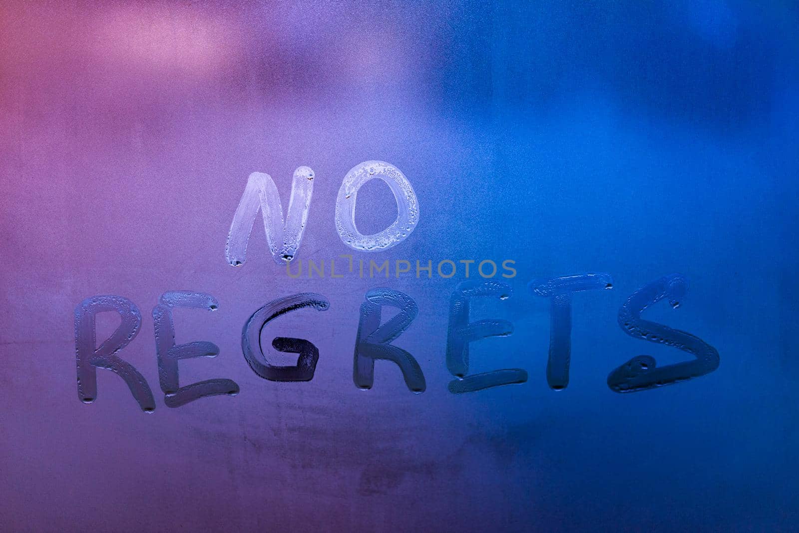 words no regrets hand written on purple-blue night foggy window glass - closeup with selective focus abstract concept