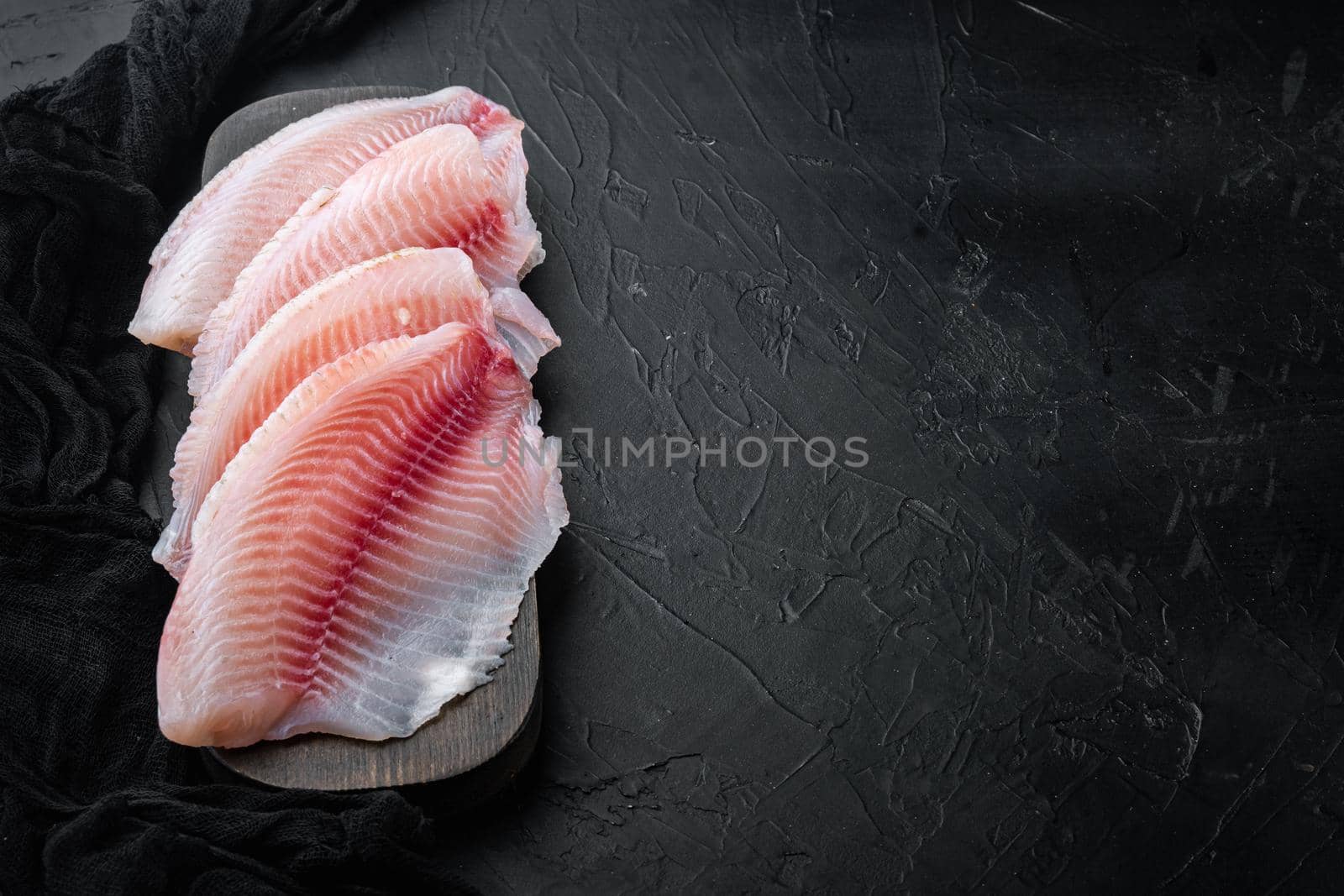 Tilapia fish, skinless meat, on black background with copy space for text