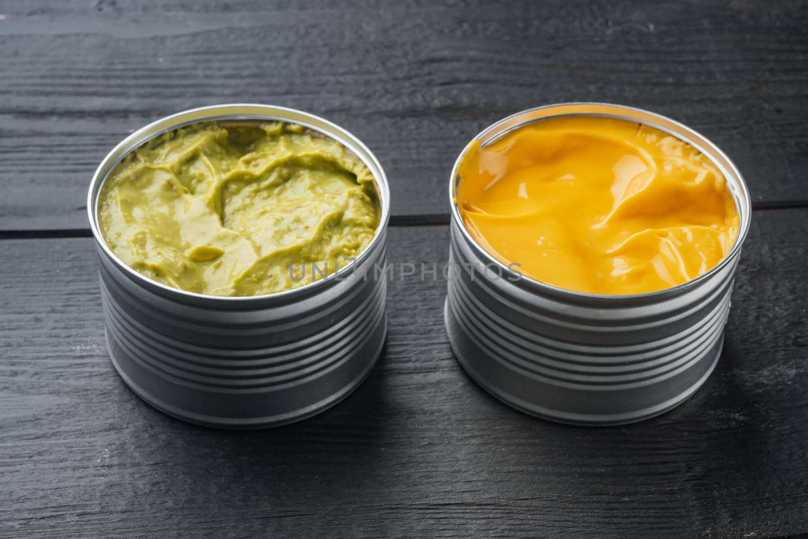 Canned cheese and guacamole sauce in can, on black wooden background