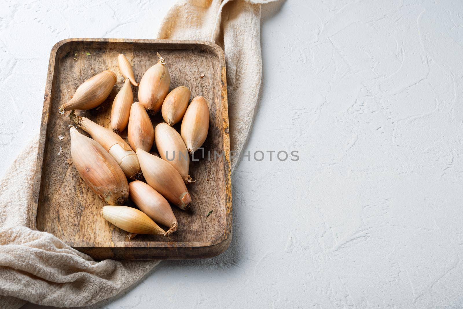 Raw whole baby shallot onion, on white textured background with space for text
