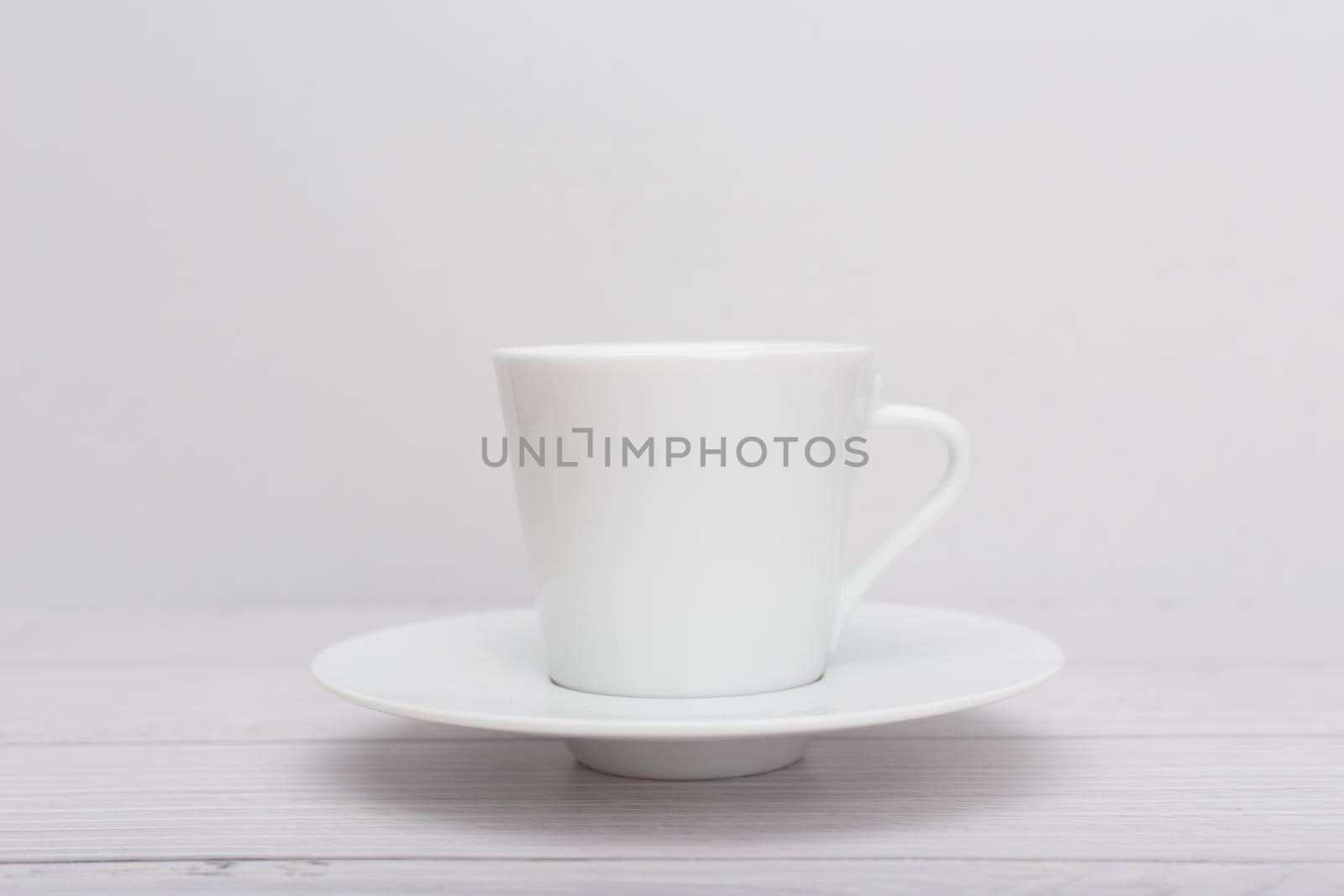 Selective focus, white ceramic tea or coffee cup with a saucer on white wooden table against white blurry background. High quality photo
