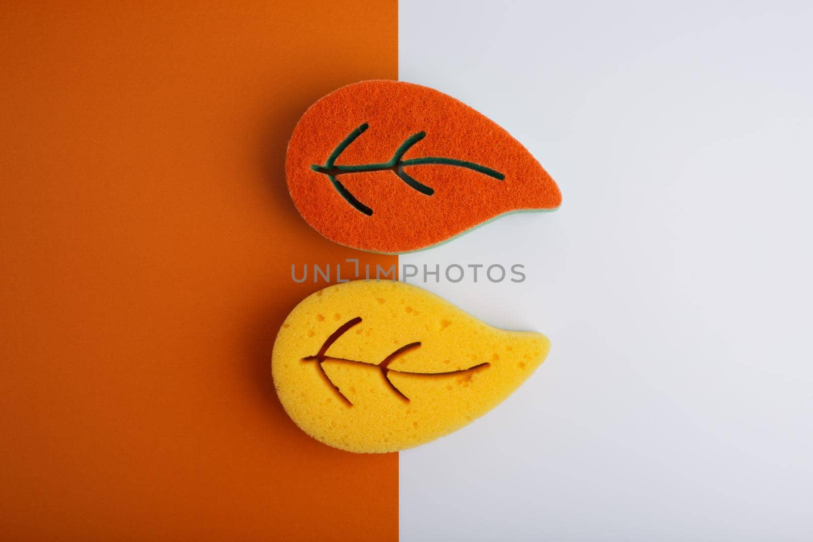 Flat lay with orange and yellow leaf shaped sponges for home and dishes cleaning on orange and white background by Senorina_Irina