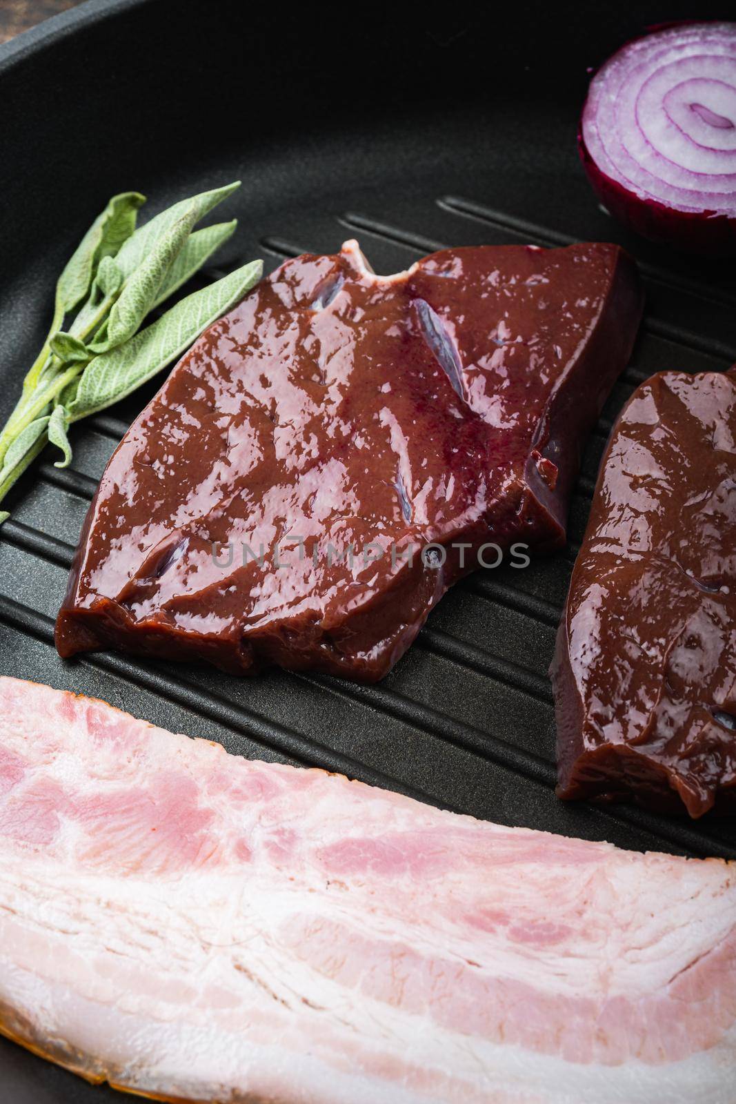 Raw beef liver sliced with bacon on grill pan over rustic background.