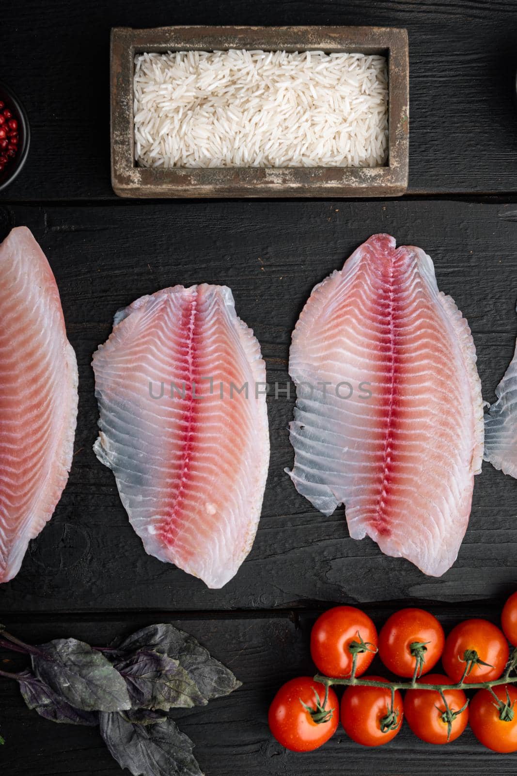 White fish fillet, with basmati rice and cherry tomatoes ingredients, on black wooden table, top view