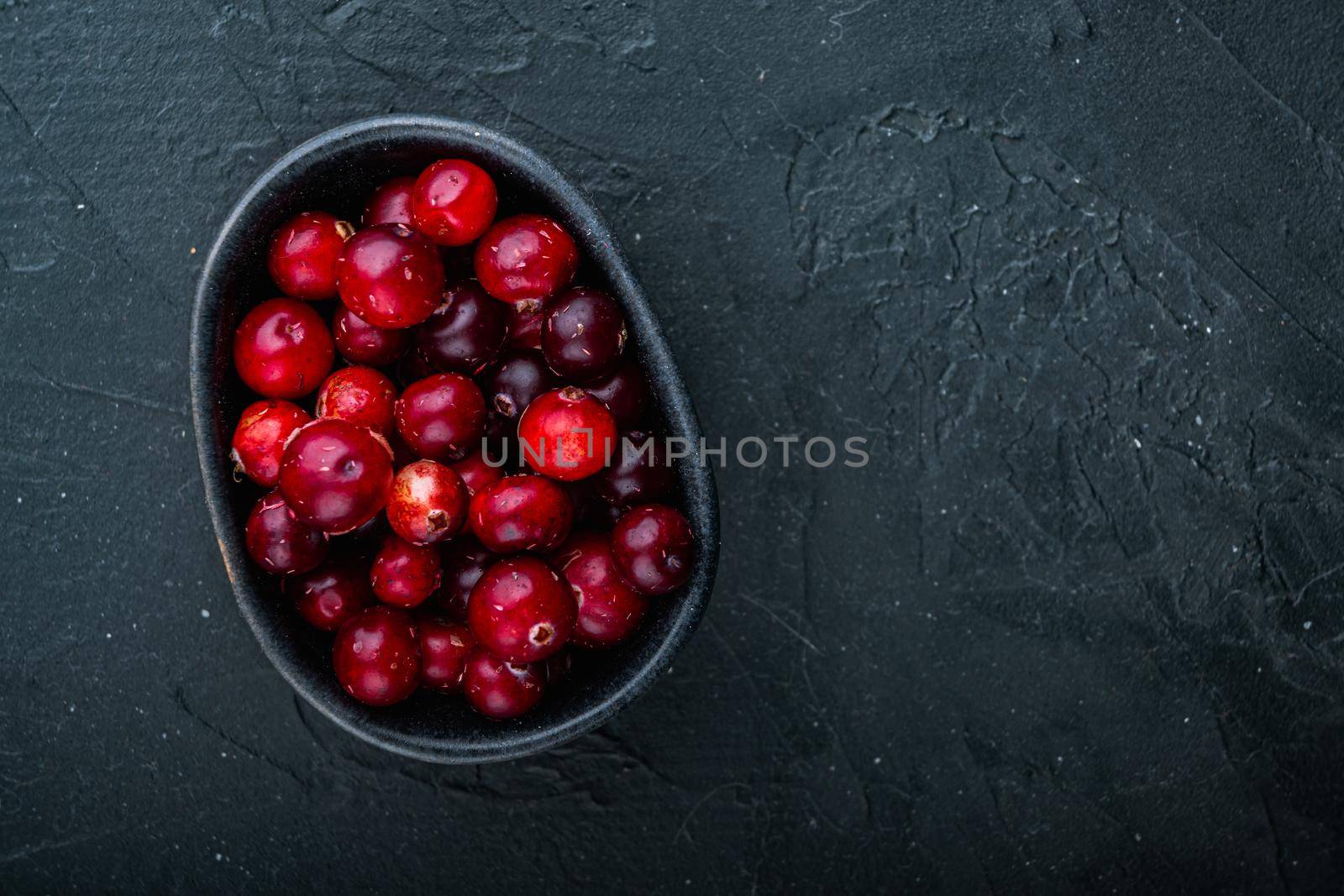 Cranberry, ripe red berry in bowl, flat lay with space for text, on black background.