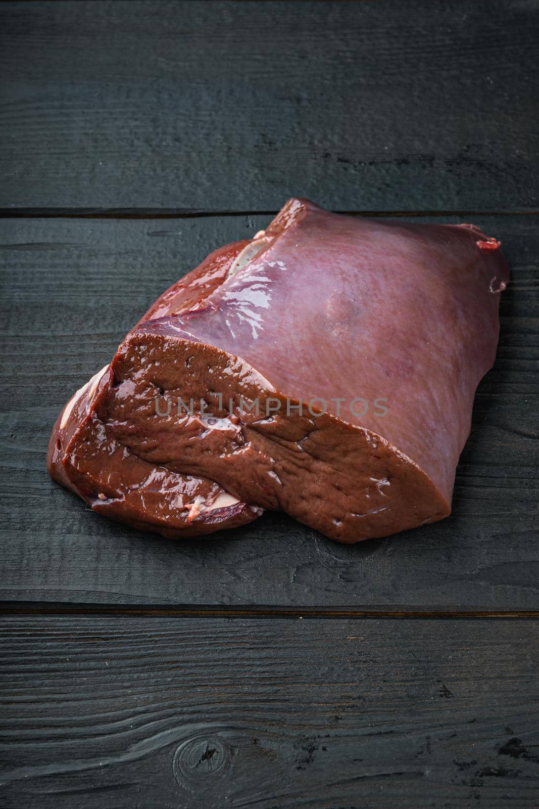 Raw liver on black wooden background with copy space.