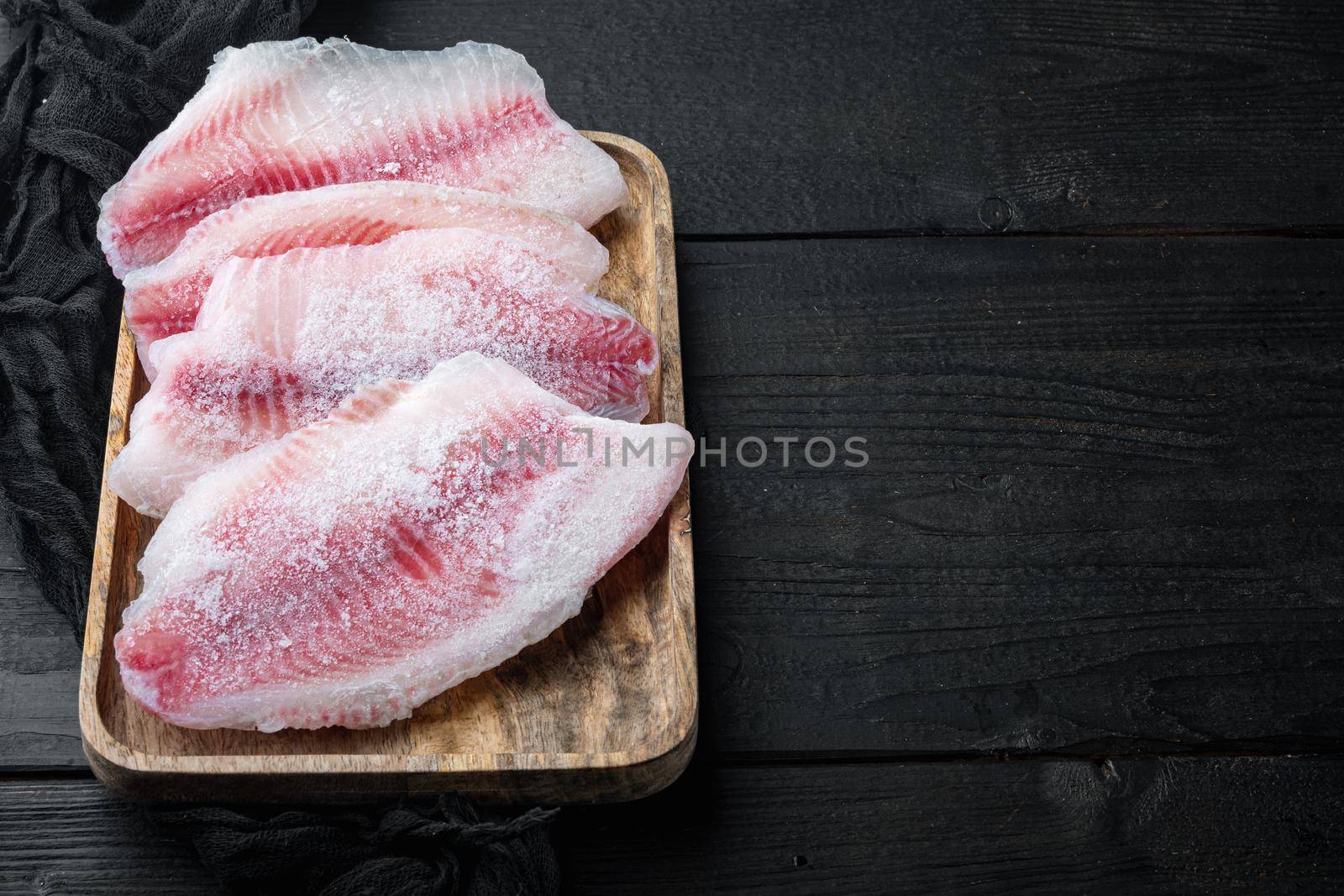 Frozen, white fish fillet, on black wooden background with copy space for text