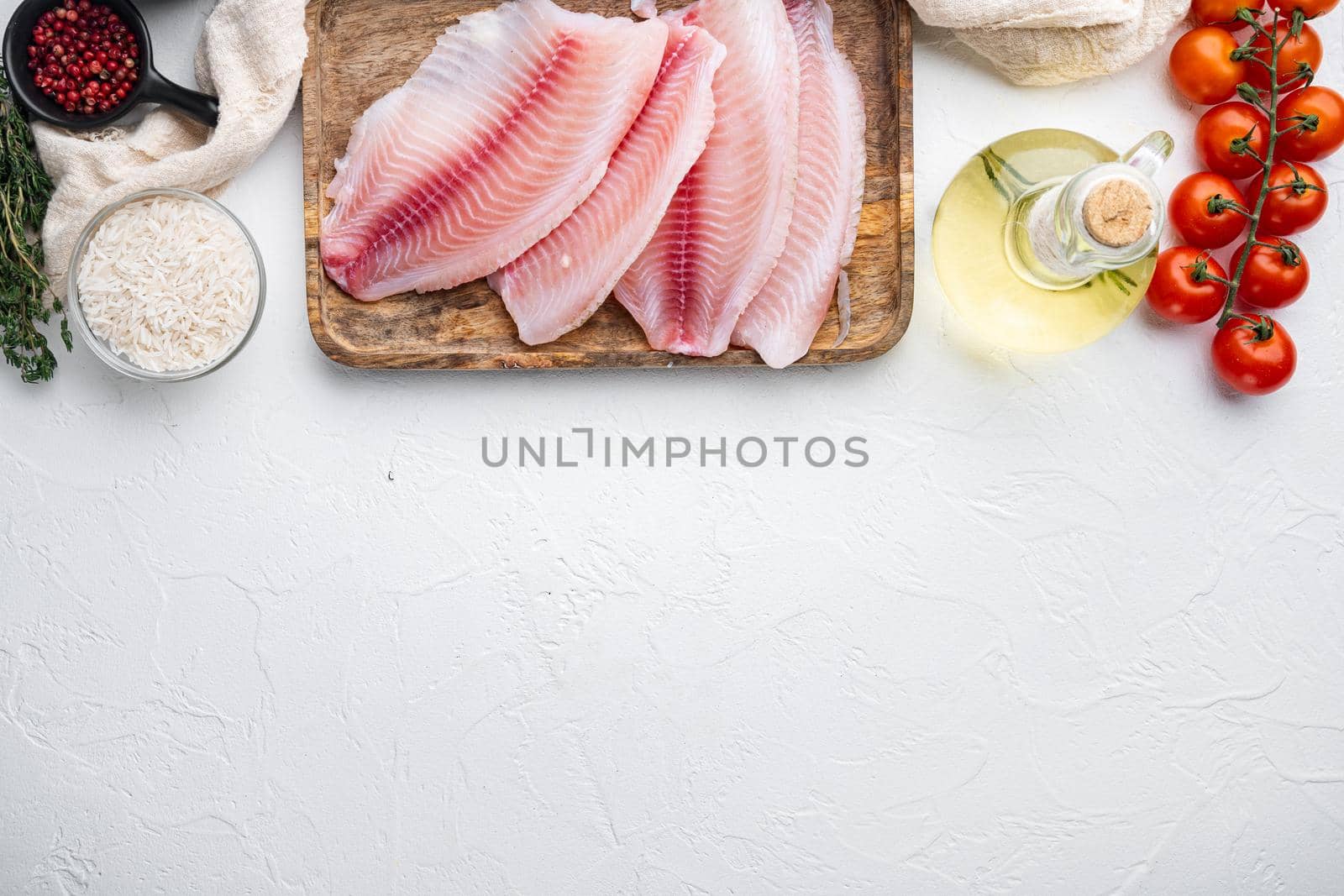 Raw white fish tilapia, with basmati rice and cherry tomatoes ingredients, on white background, top view with copy space for text