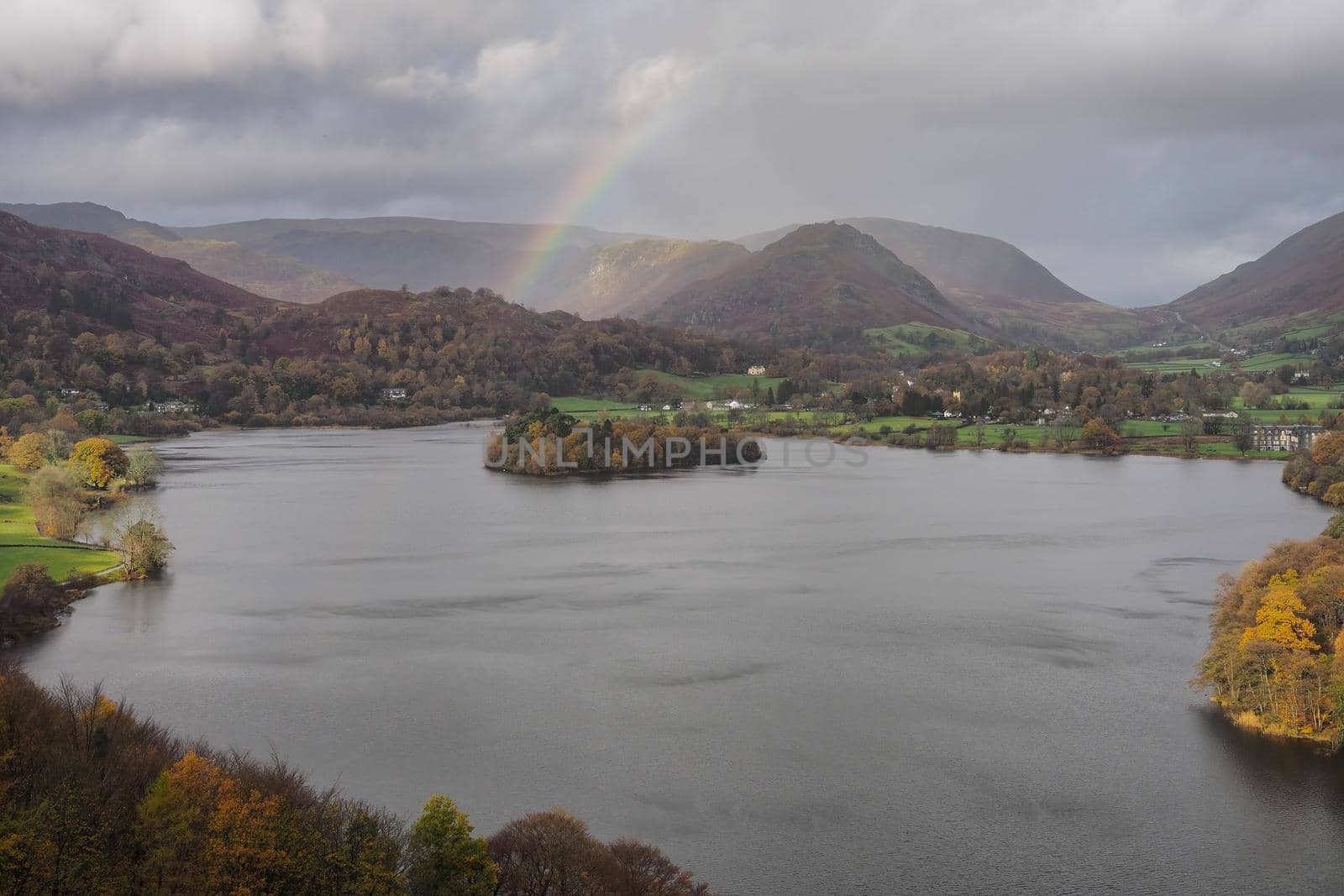 View climbing up Loughrigg Fell over the lake of Grasmere with a rainbow arcing across the fells under a stormy sky, Lake District, UK