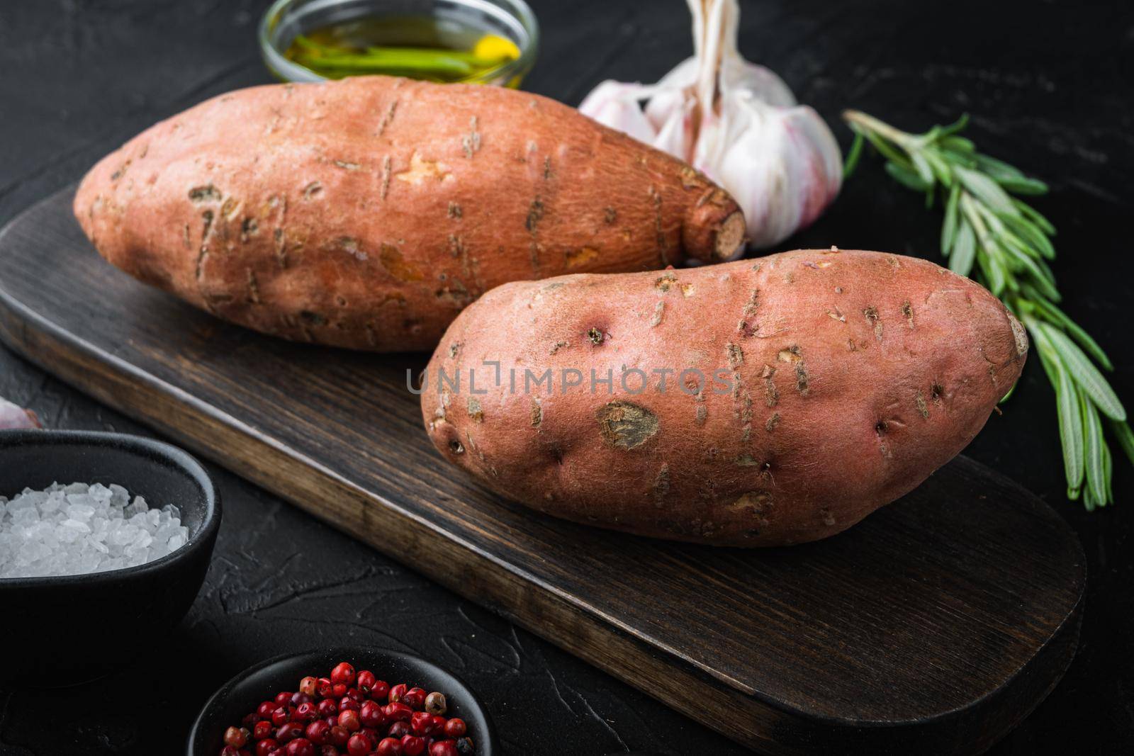 Sweet potato or batat with herbs and spices on black background.