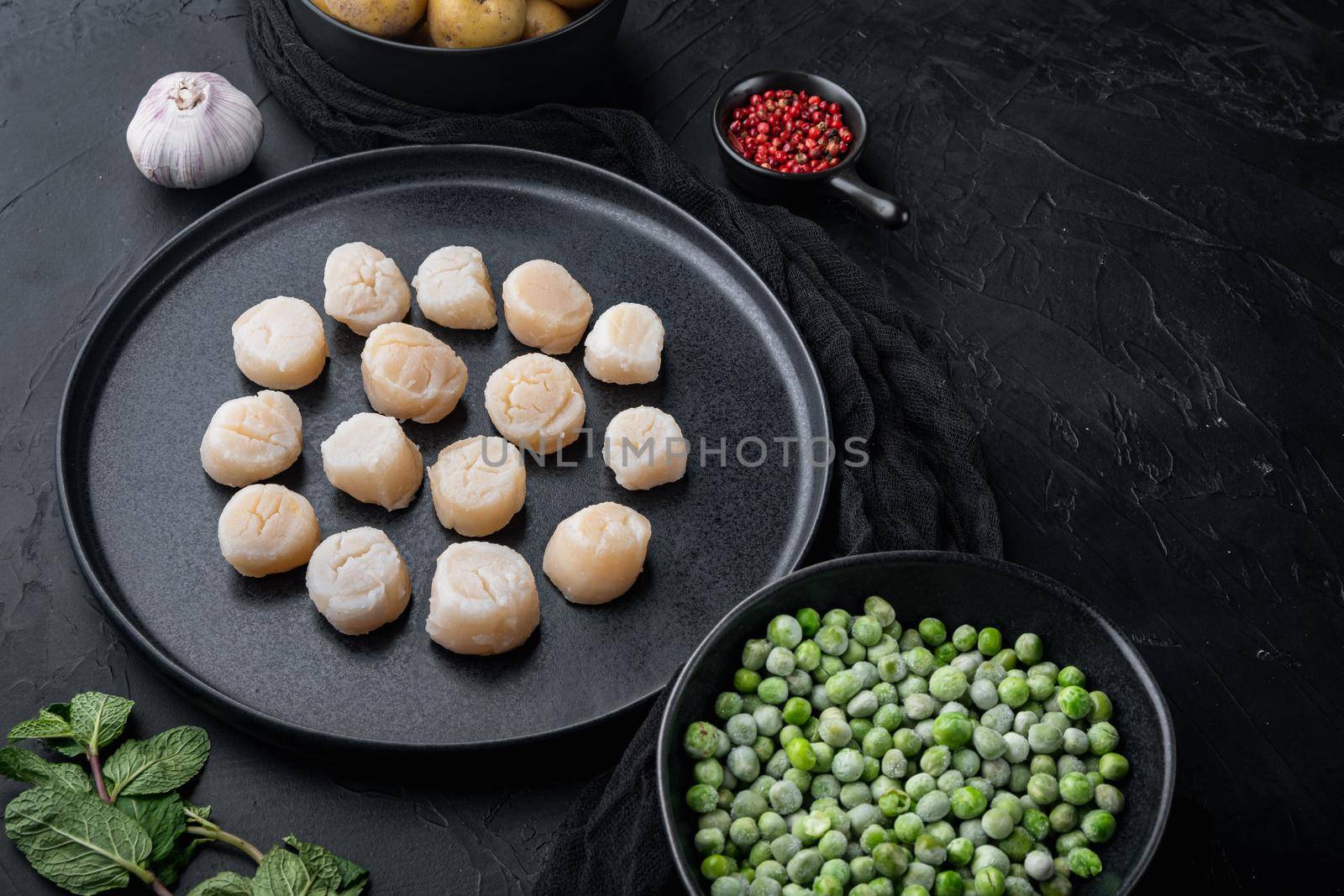 Fresh seafood scallops with herbs and vegetables, on black textured background with space for text