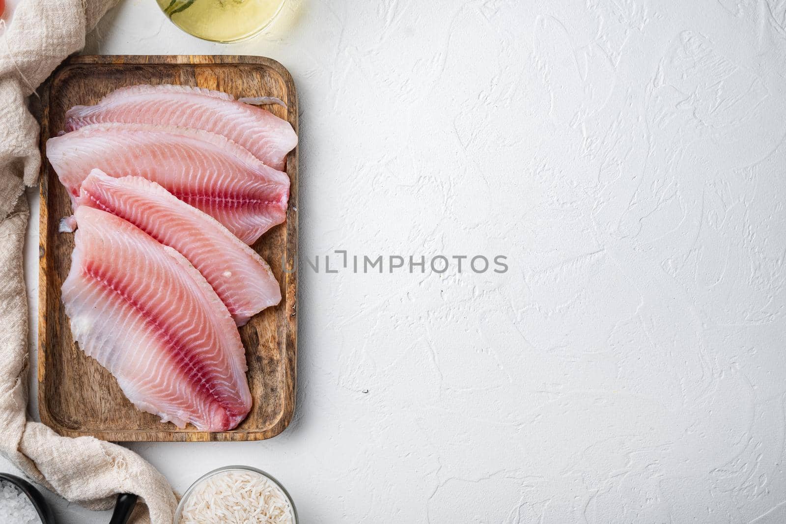 Raw white fish tilapia, with basmati rice and cherry tomatoes ingredients, on white background, top view with copy space for text