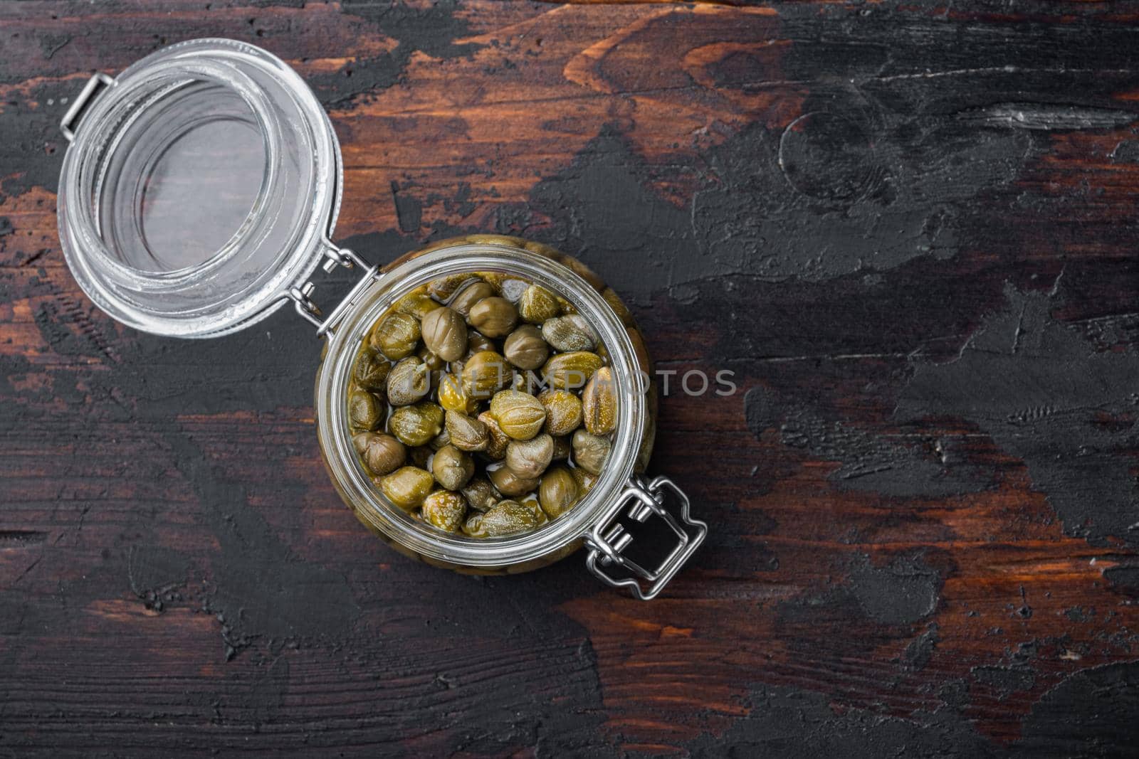 Baby capers in marinate glass jar, on old wooden table, top view with copy space for text