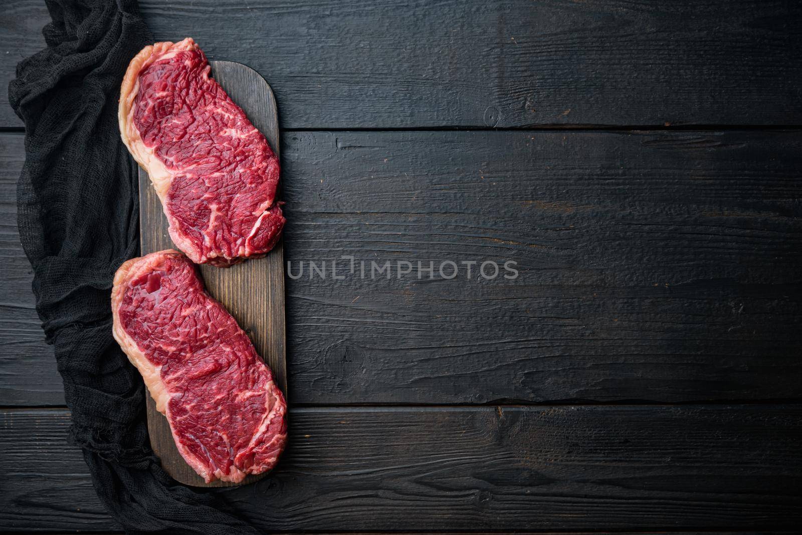 Strip loin steak, raw marbled beef meat, on black wooden table, top view, with copy space for text
