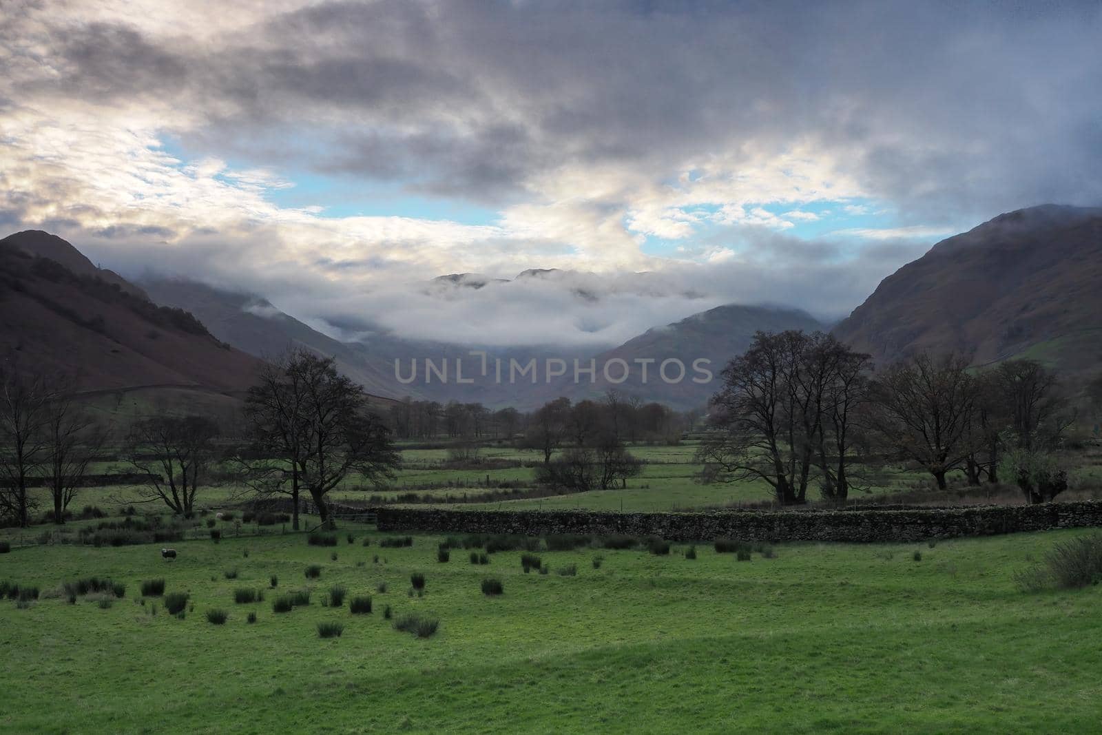 View across the fields to the Langdale Pikes at sunset as the clouds started to part over the peaks, Lake District, UK