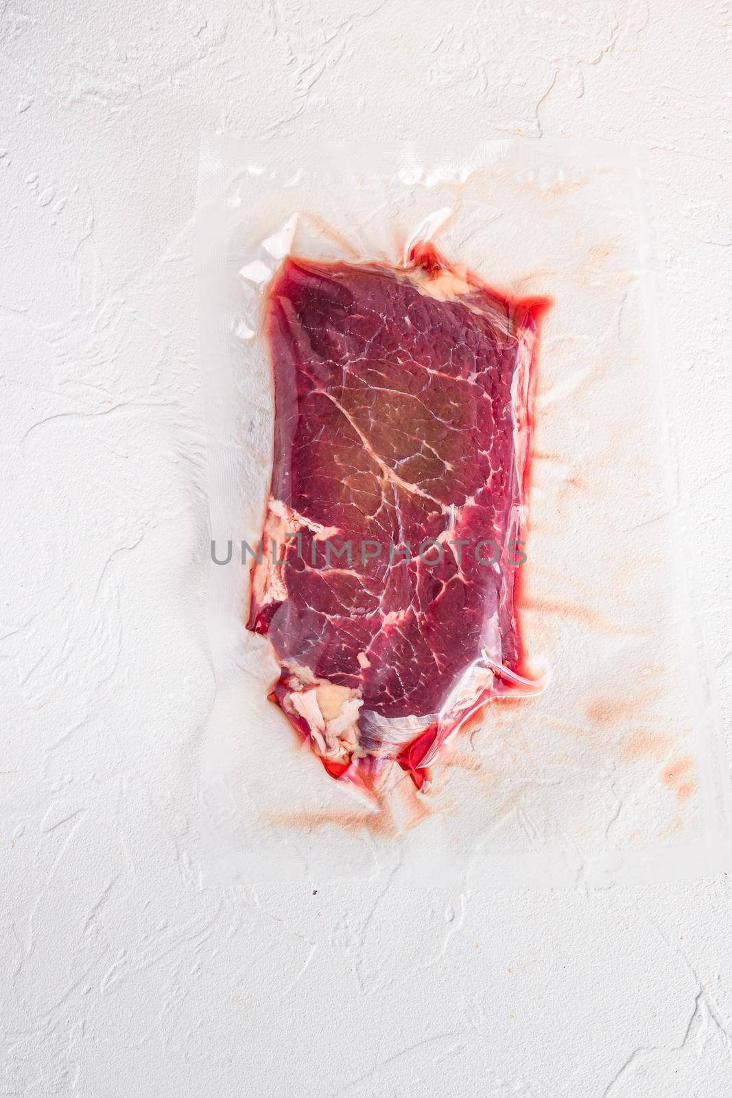 Raw rump beef steak, vacuum packed organic meat for sous vide cooking on white concrete textured background, top view