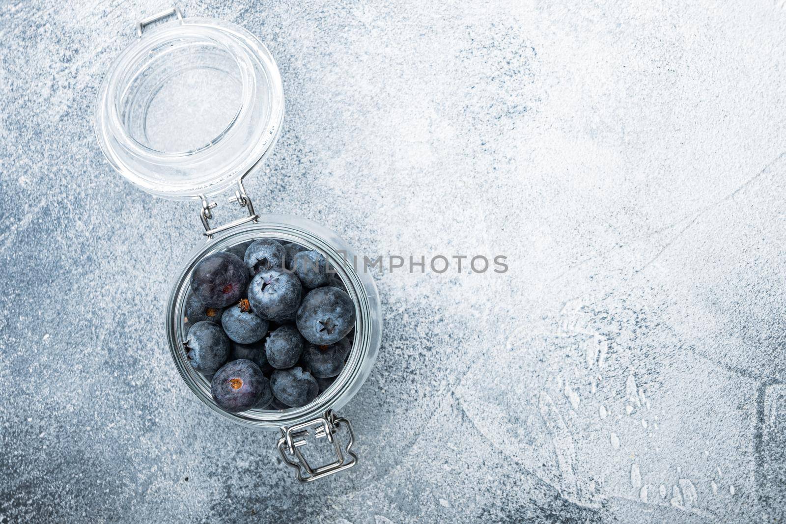 Ripe blueberry in glass jar, flat lay with space for text, on textured background.