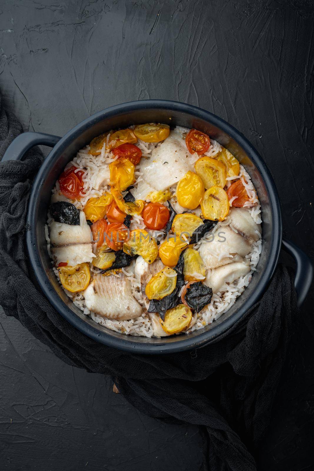 White tilapia fish, with basmati rice and cherry tomatoes, on black background, top view