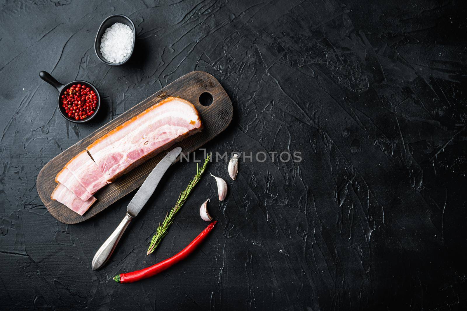 Smoked bacon, whole slab with herbs on black background, top view with space for text.