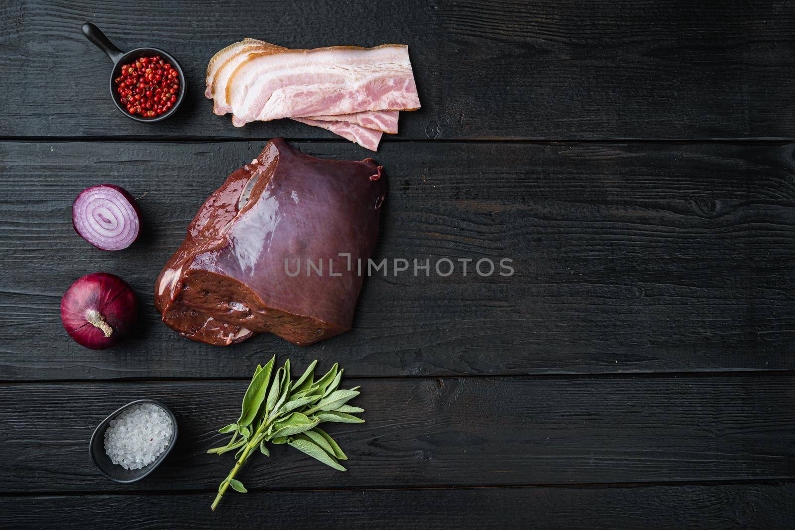 Raw liver with bacon and onion on black wooden background, flat lay with copy space.