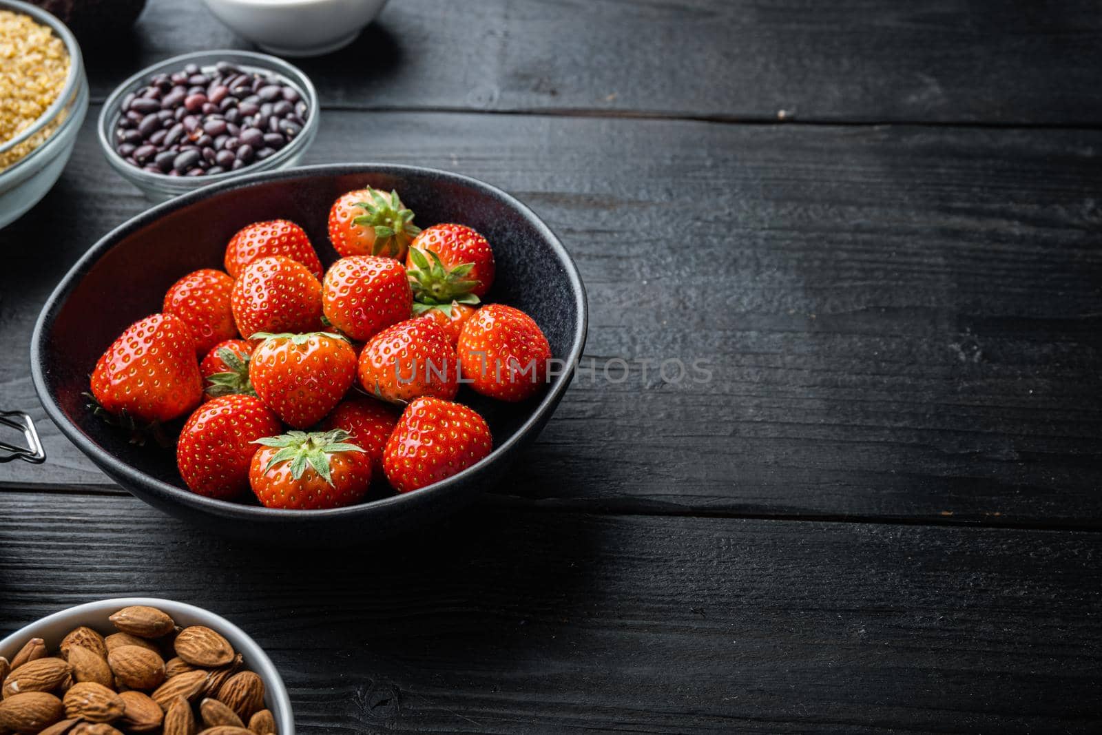 Ripe red strawberry with space for text, on black wooden background.