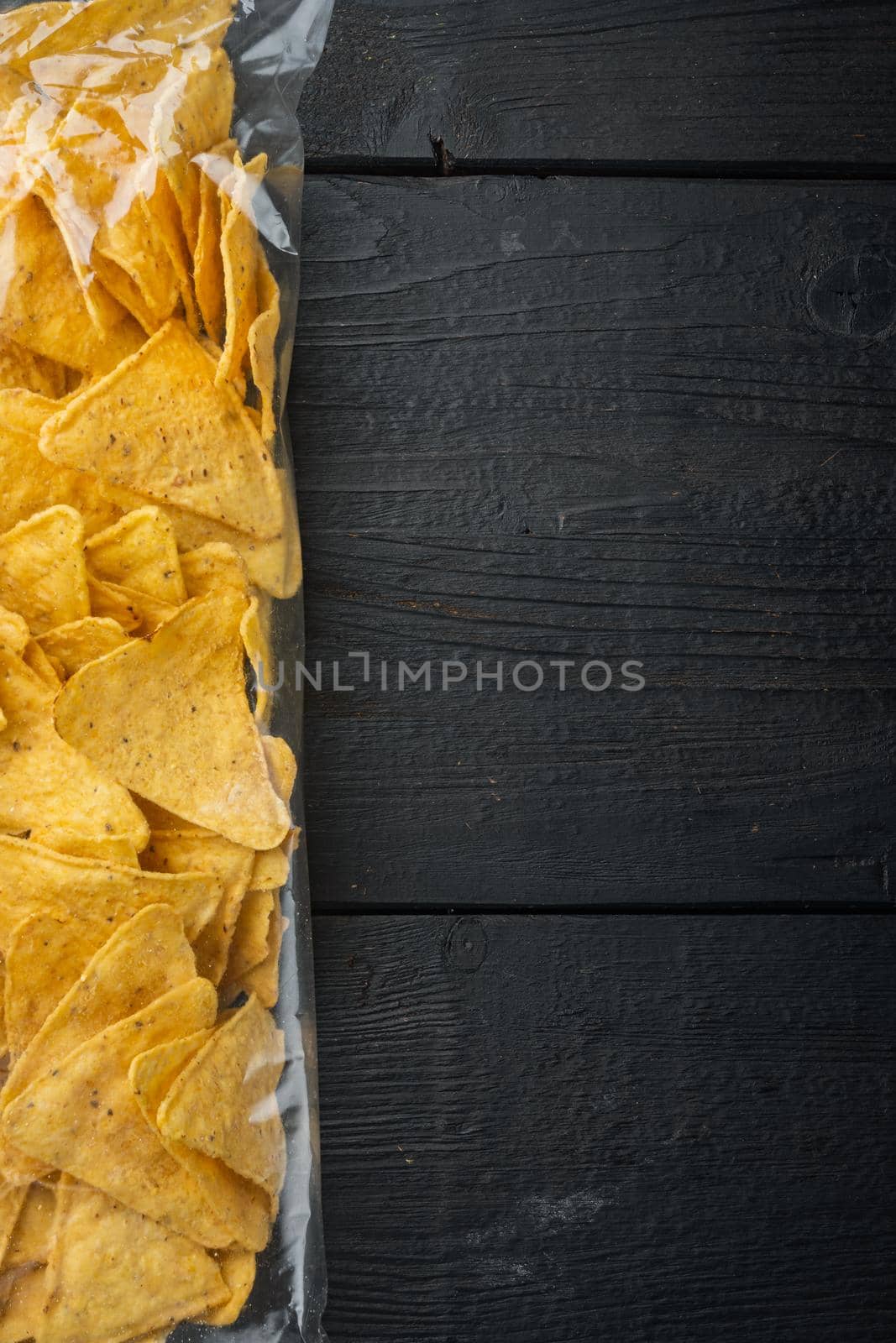 Nachos, corn tortilla in bag, on black wooden background, top view or flat lay with copy space for text
