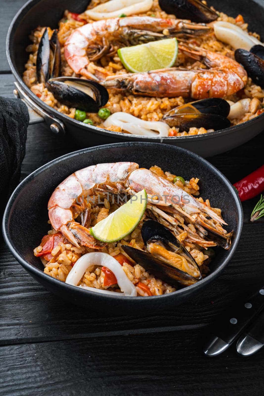 Typical spanish seafood paella in traditional pan and black bowl on black wooden background, food photo.