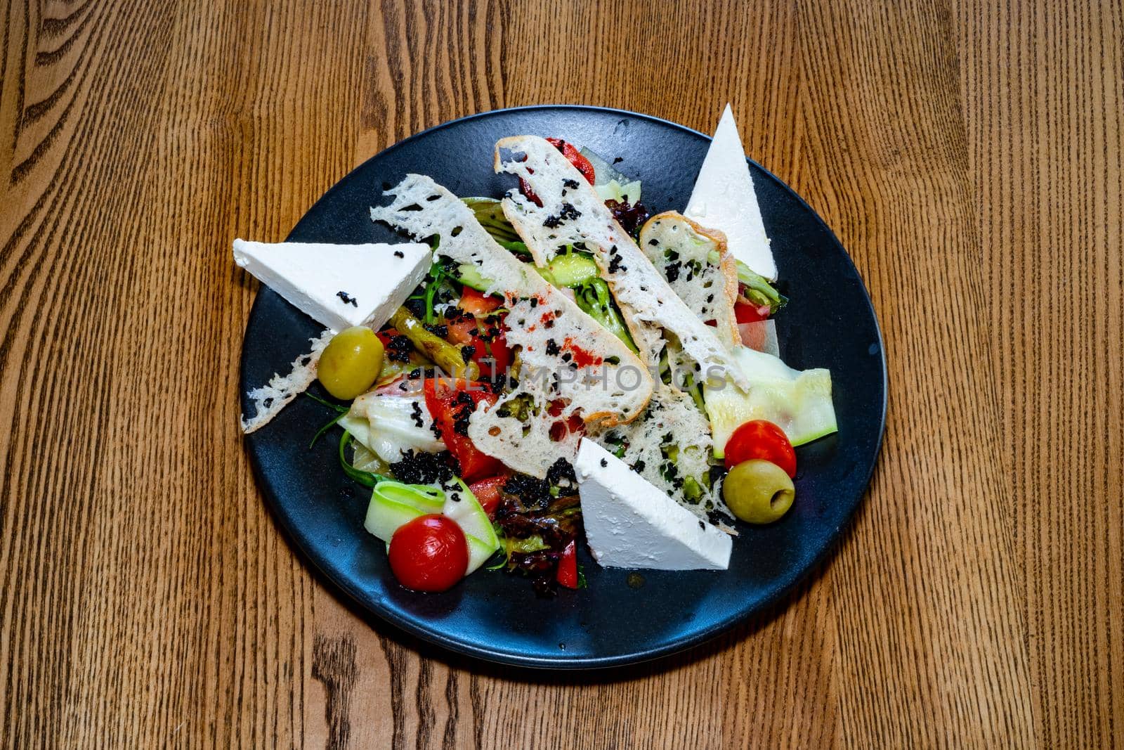 Salad on a plate. Salad with cheese, bread, ofochas and fruits on a black plate.