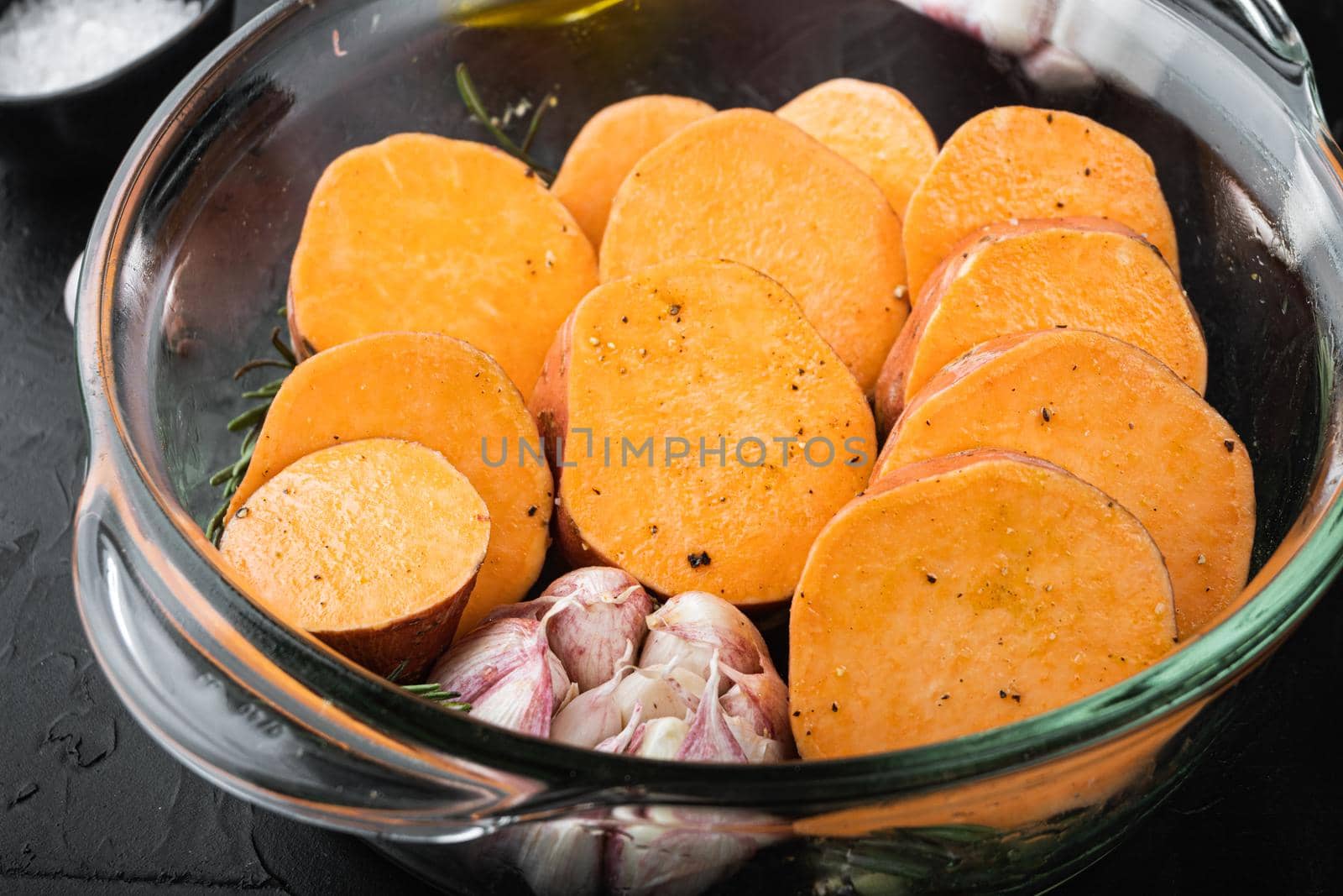 Cajun sweet potatoes for baking with herbs and spices on black background.