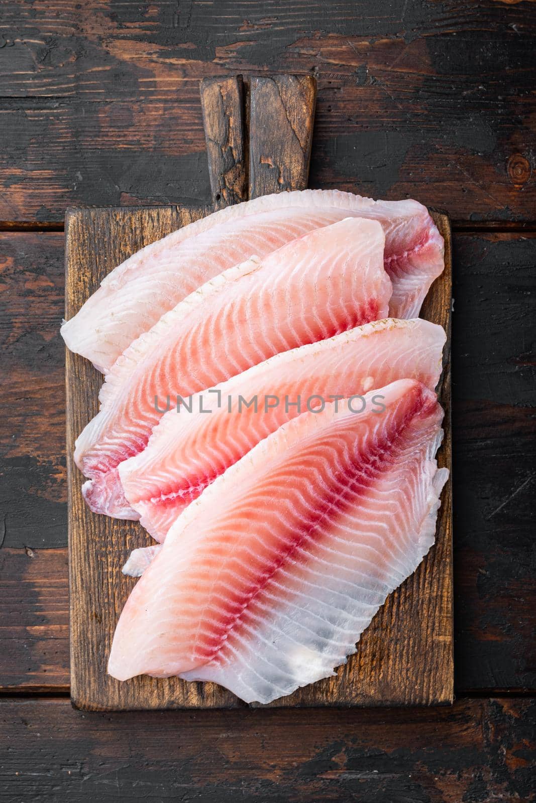 Tilapia fish skinless meat, on dark wooden background, top view by Ilianesolenyi