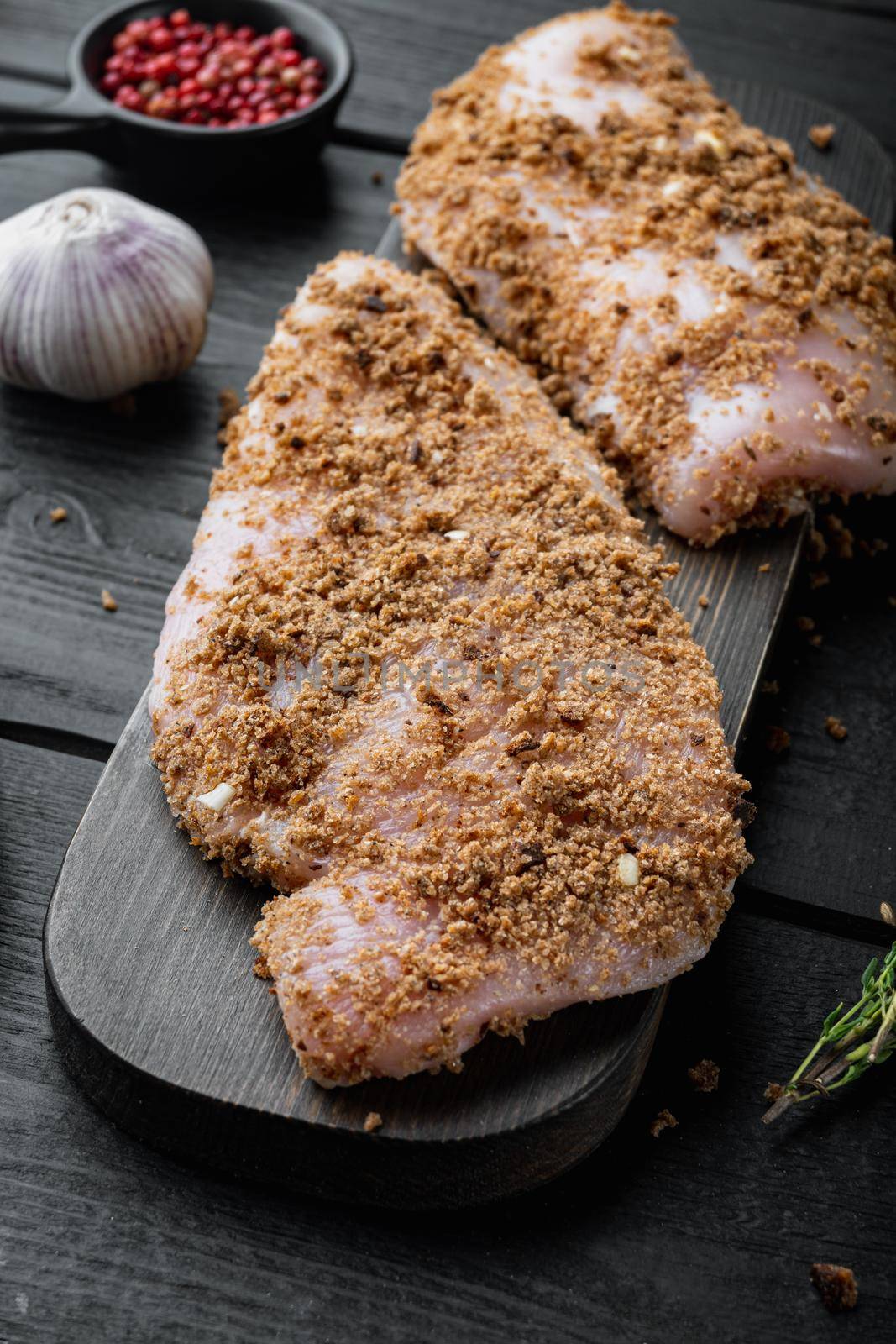 Crumbed uncooked chicken breast ingredient, on black wooden background by Ilianesolenyi