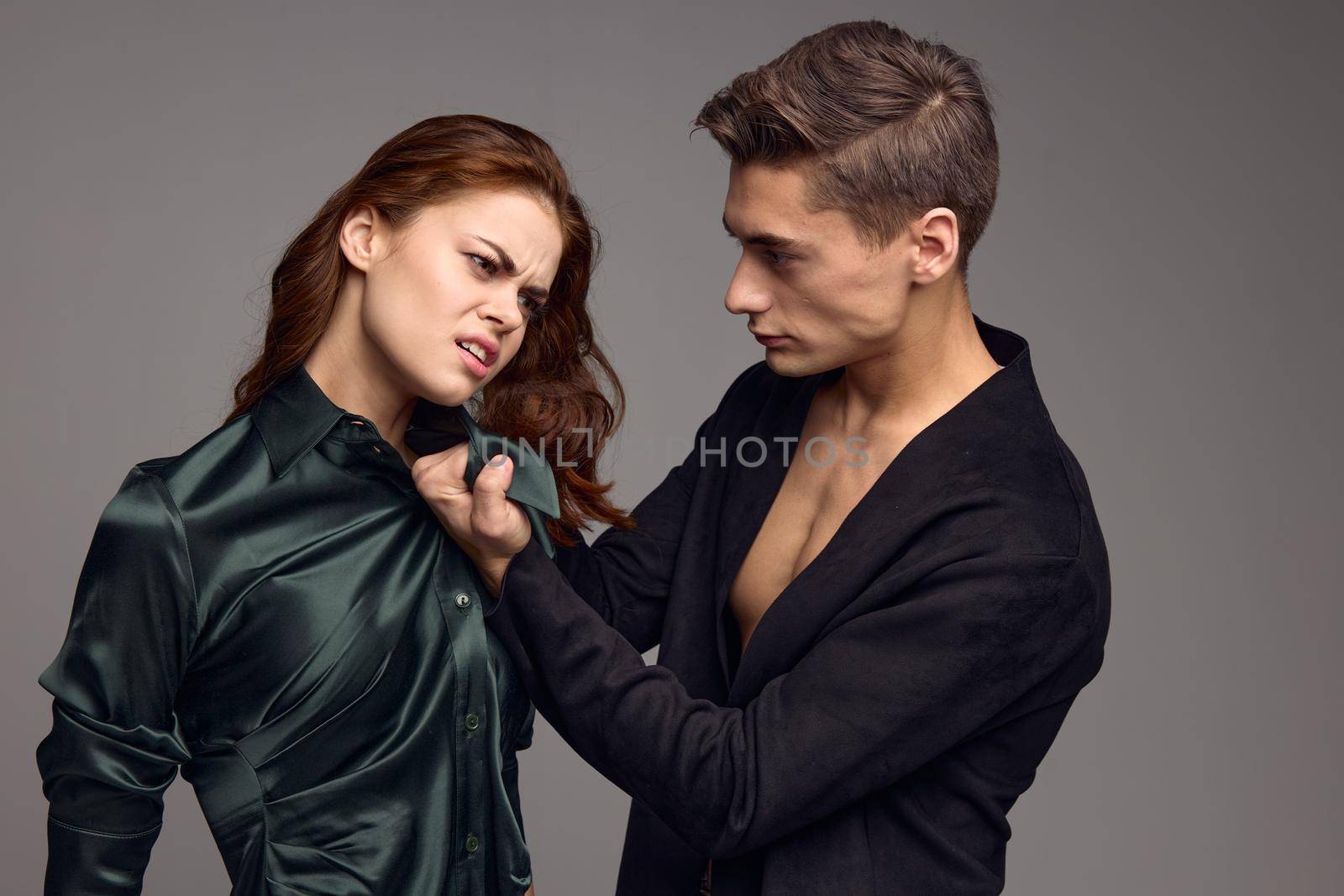 A man holds a woman by the collar causing her pain and on a gray background. High quality photo