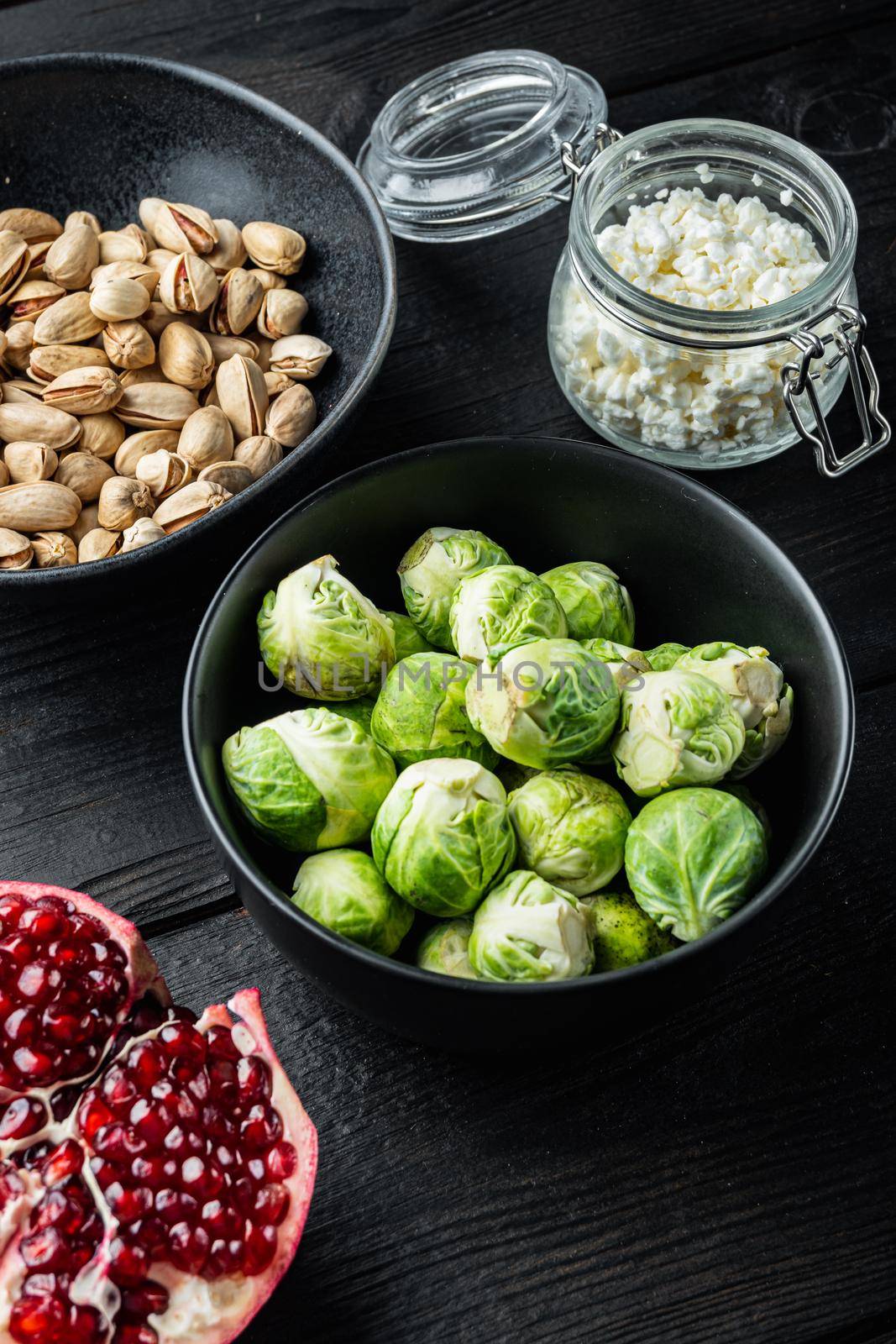 Brussels sprouts, with pomegranate, cottage cheese and pistachios, on black wooden table by Ilianesolenyi