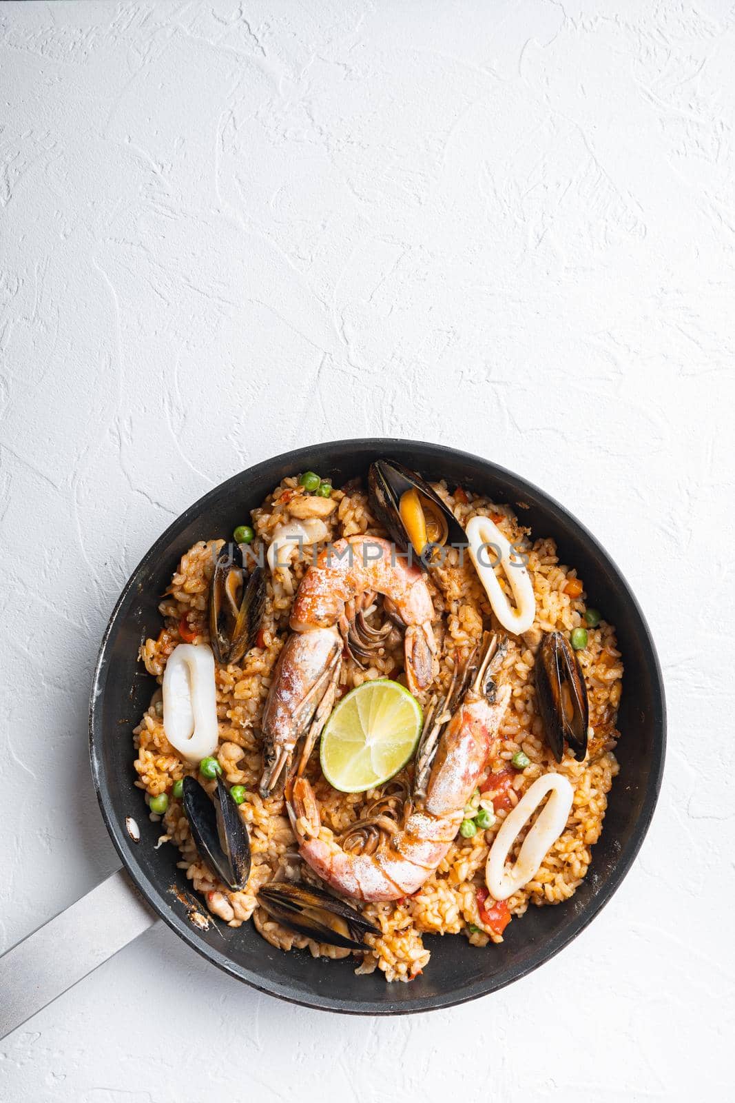 Seafood and chicken paella with rice, mussles, shrimps,chicken, tomatoes and wine in pan on white textured background, flat lay with copy space by Ilianesolenyi
