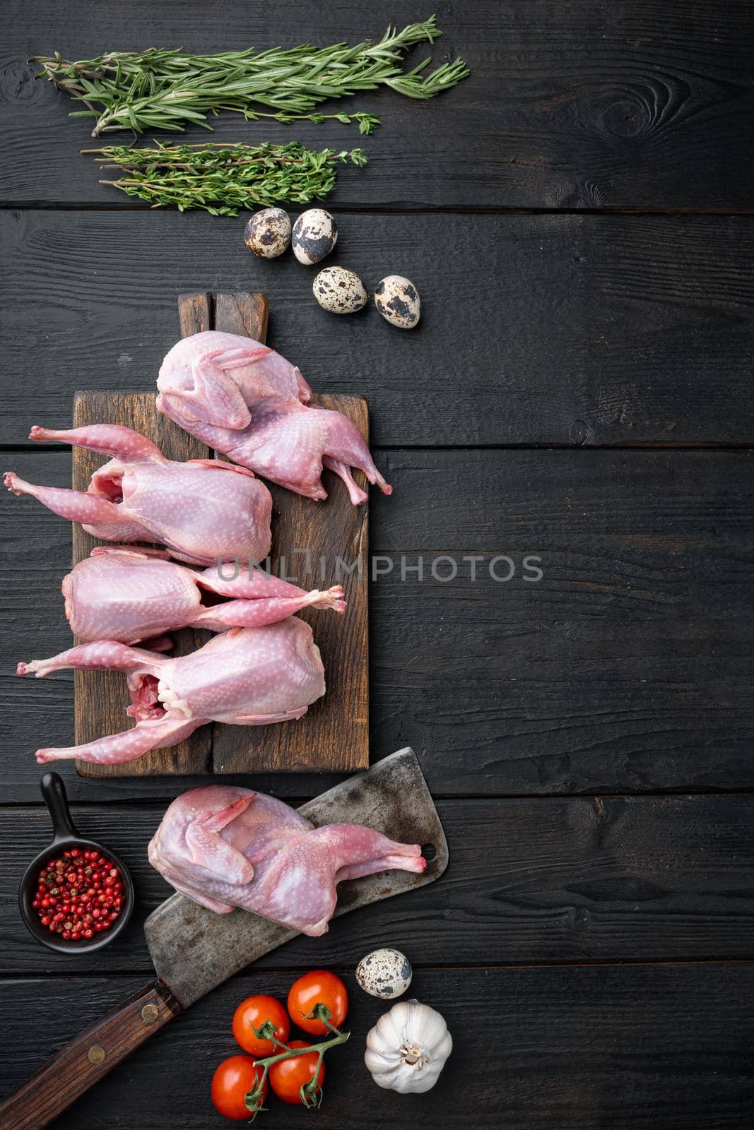 Whole quails meat with spices, herbs, vegetables, top view, on black wooden background with copy space