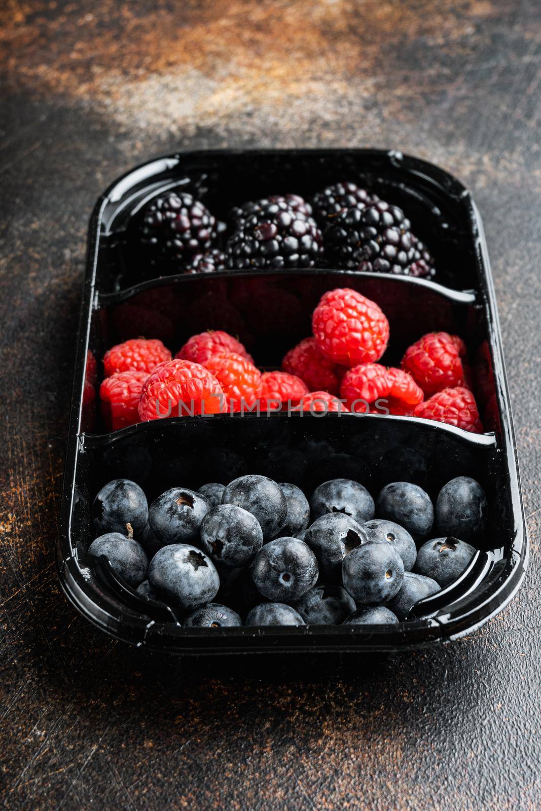 Fresh berries are packed in tray, blueberries, raspberry and blackberry, on old dark table by Ilianesolenyi