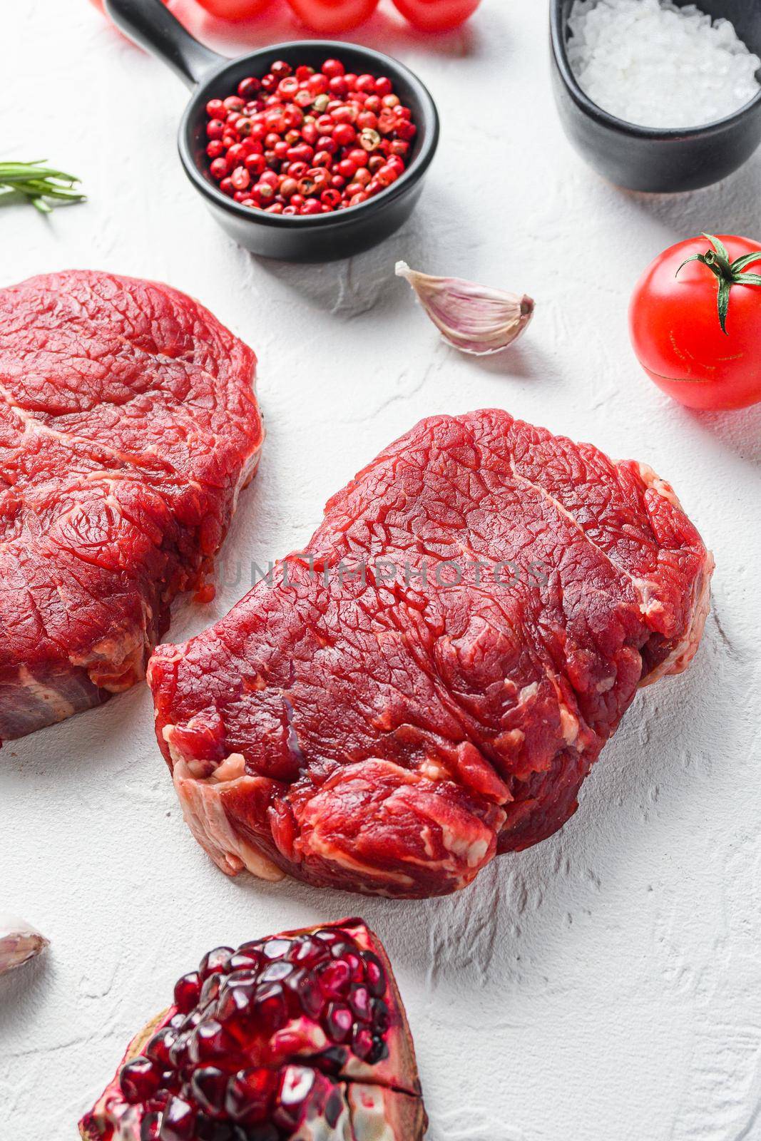 Raw rumpsteak, farm beef meat with seasonings, rosemary, garlic, garnet. White textured background. Side view. by Ilianesolenyi