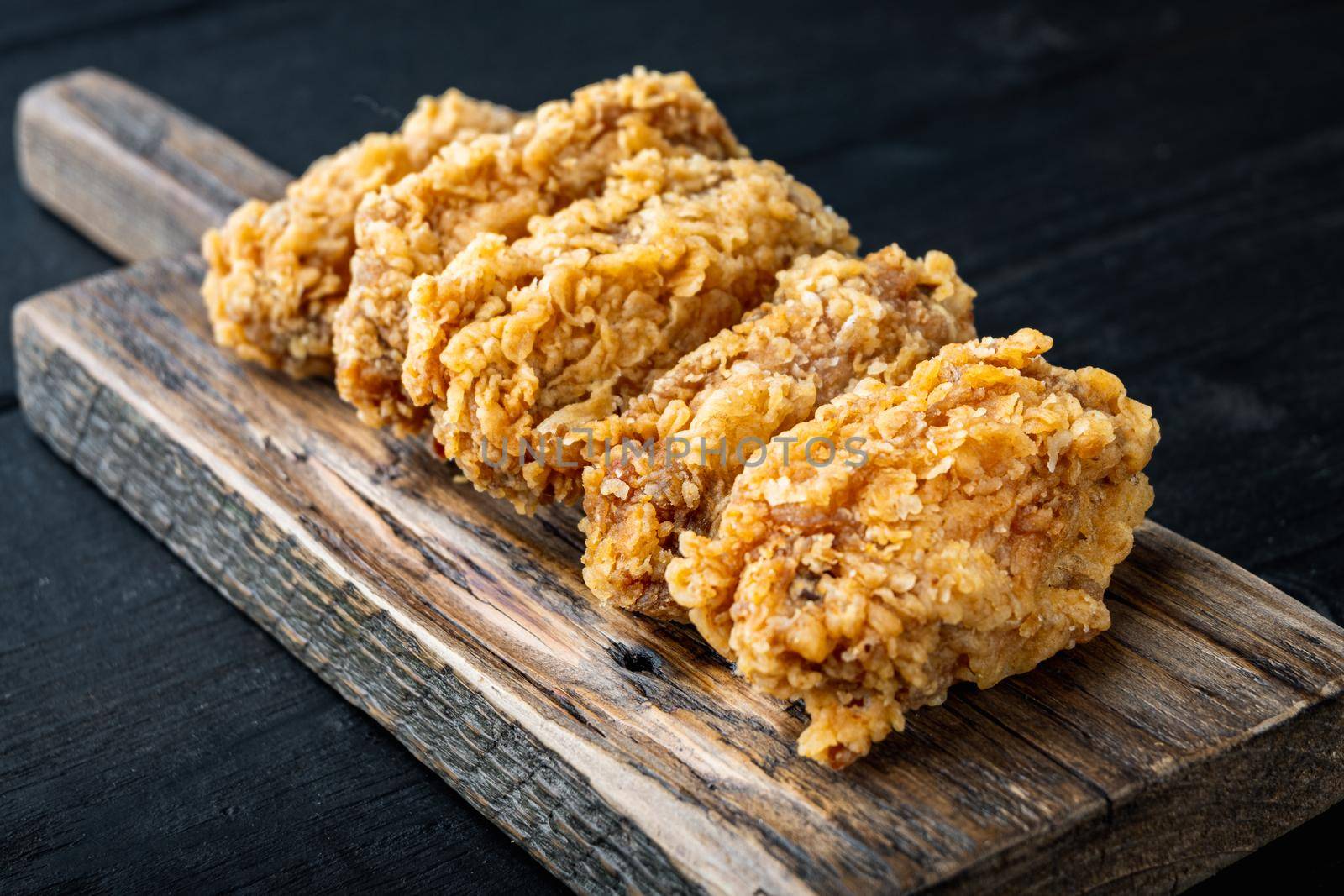 Breaded chicken wings cuts on black wooden table.