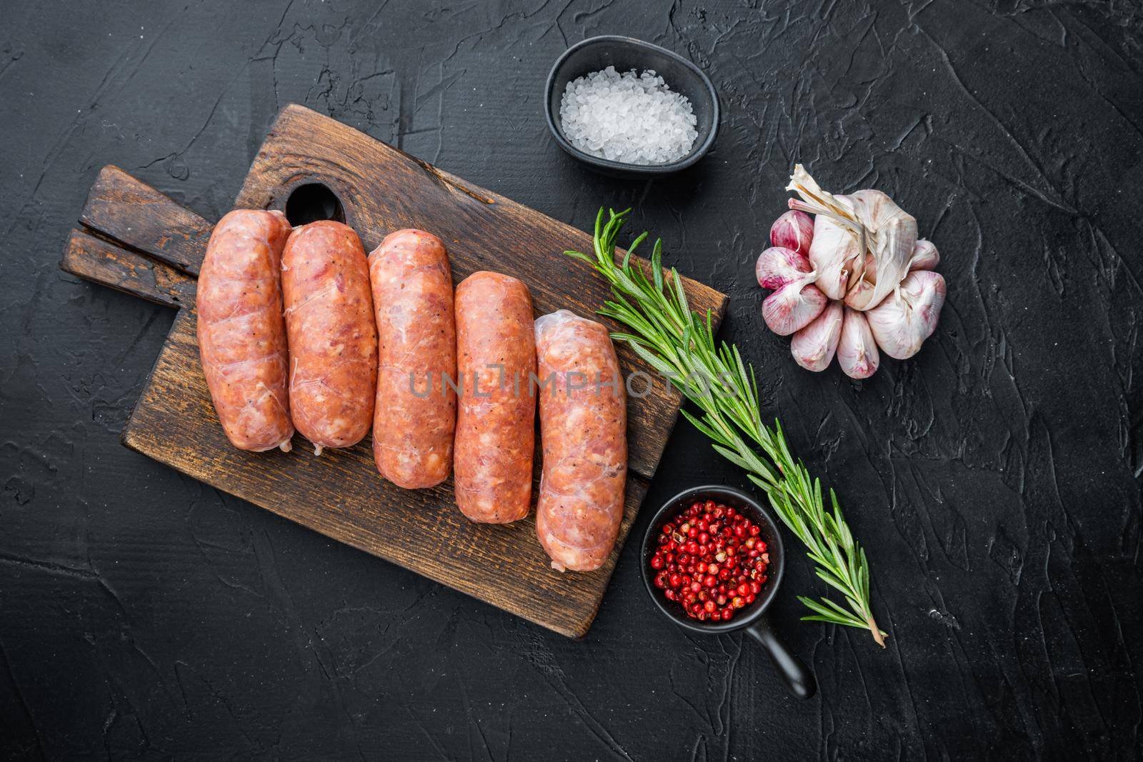 Raw organic pork sausages, top view, on black background.