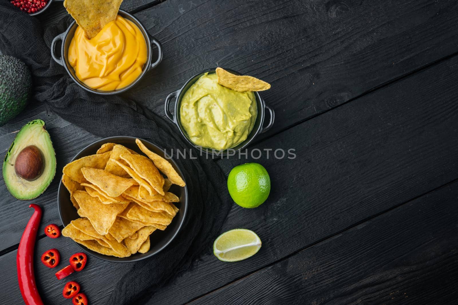 Mexican nachos chips with cheese and guacamole sauces, on black wooden background, top view or flat lay with copy space for text